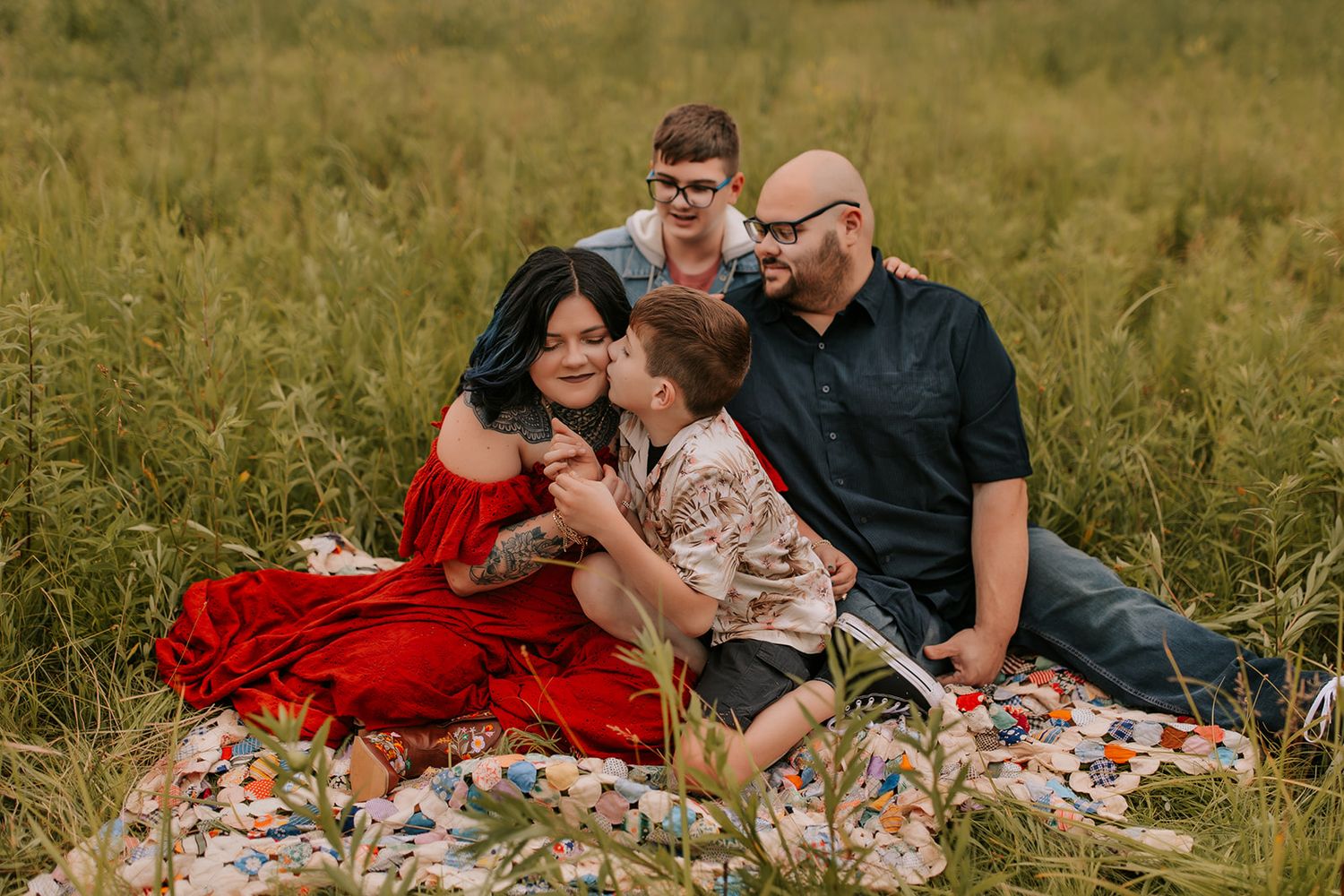 Family group relaxes on blankets in golden field during sunset photoshoot.