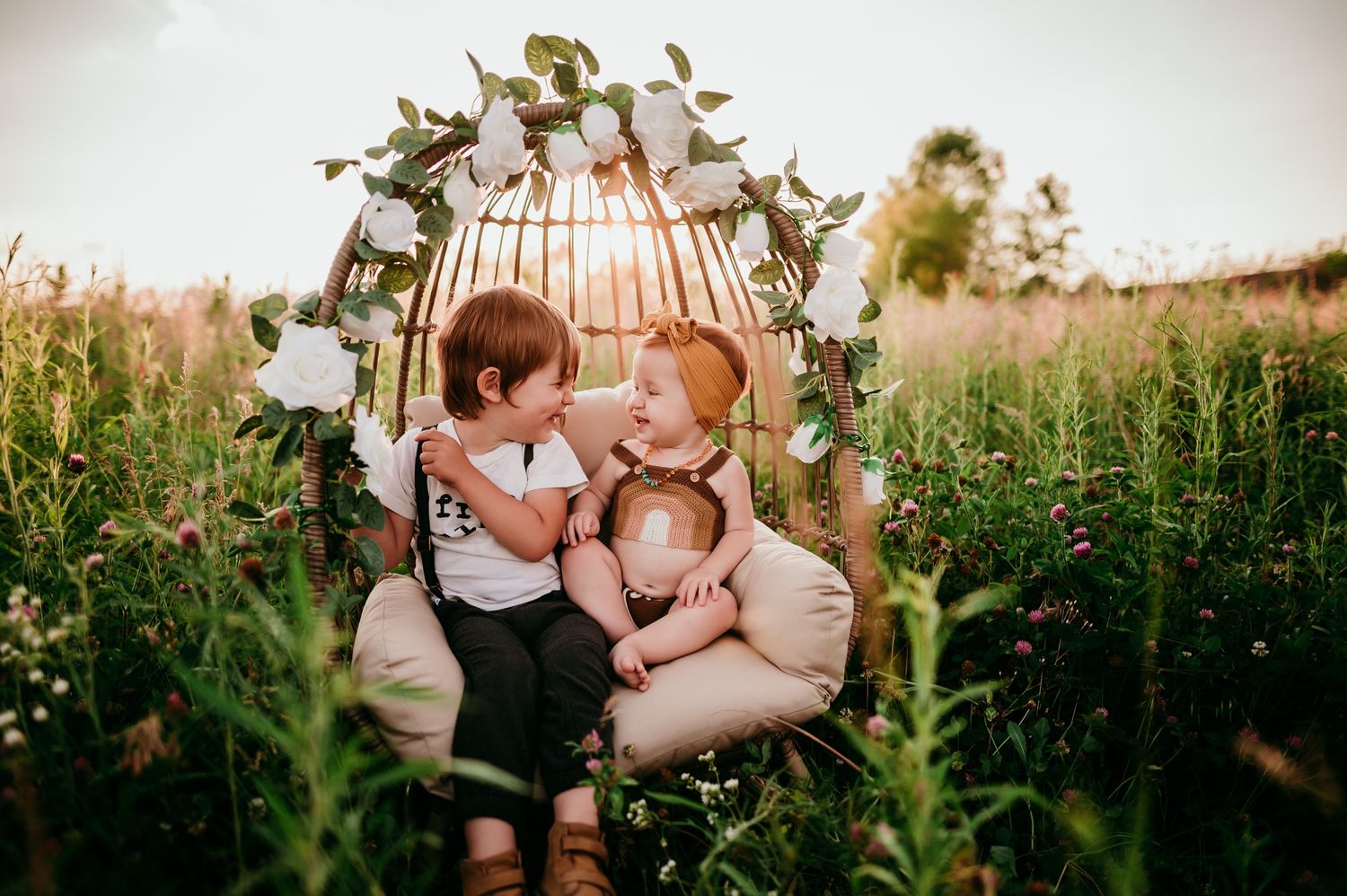 Romantic couple embraces in a sunset-lit meadow filled with wildflowers and tall grasses.