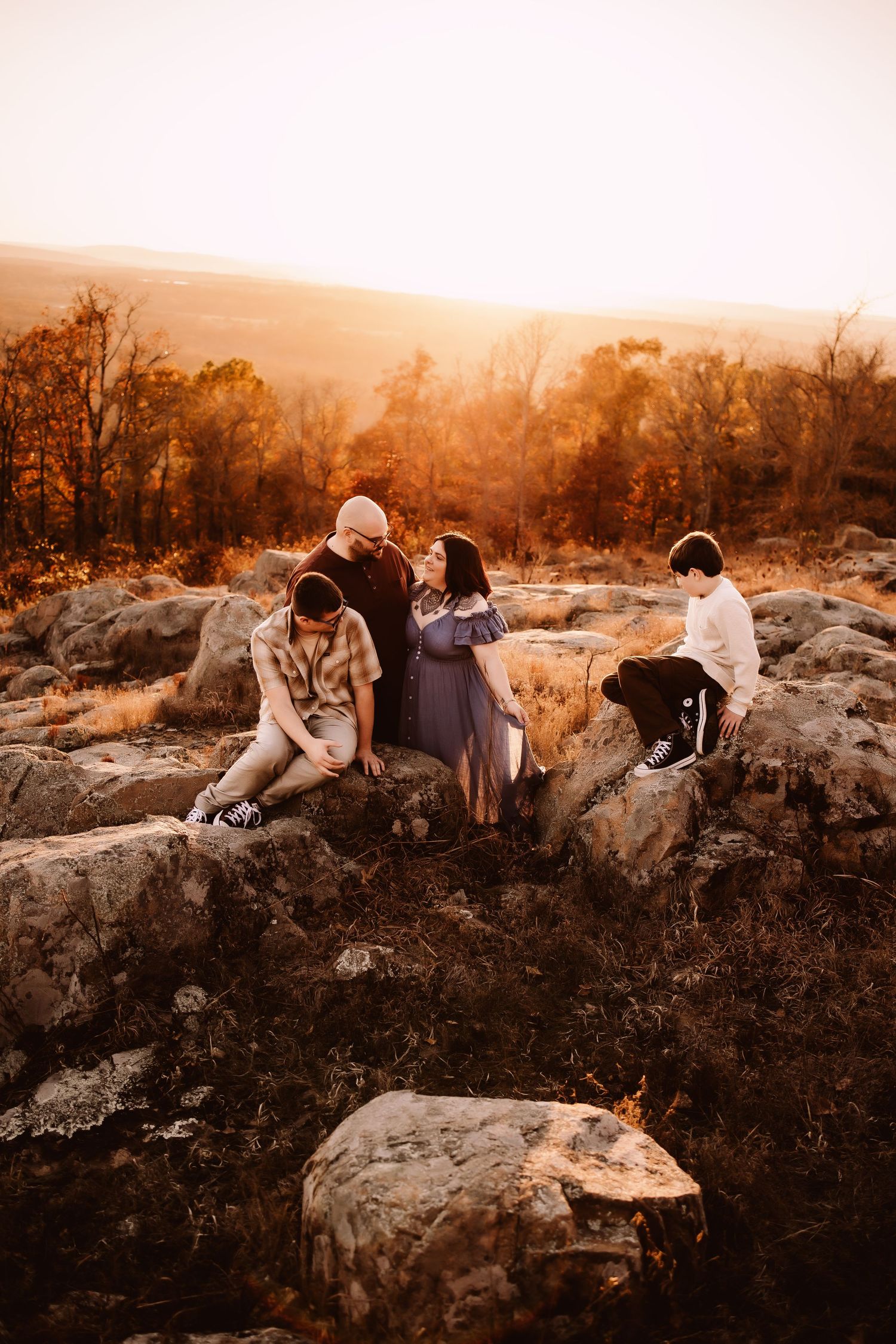 A couple sits together on rocky terrain during golden hour sunset in a warm sepia-toned photograph.