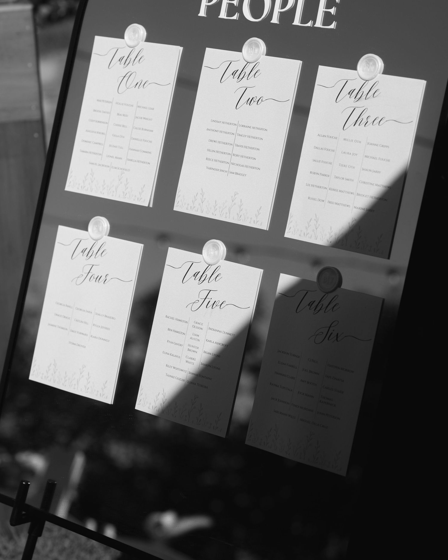 Black and white wedding seating chart showing table cards for tables one to six pinned to a mirrored sign.