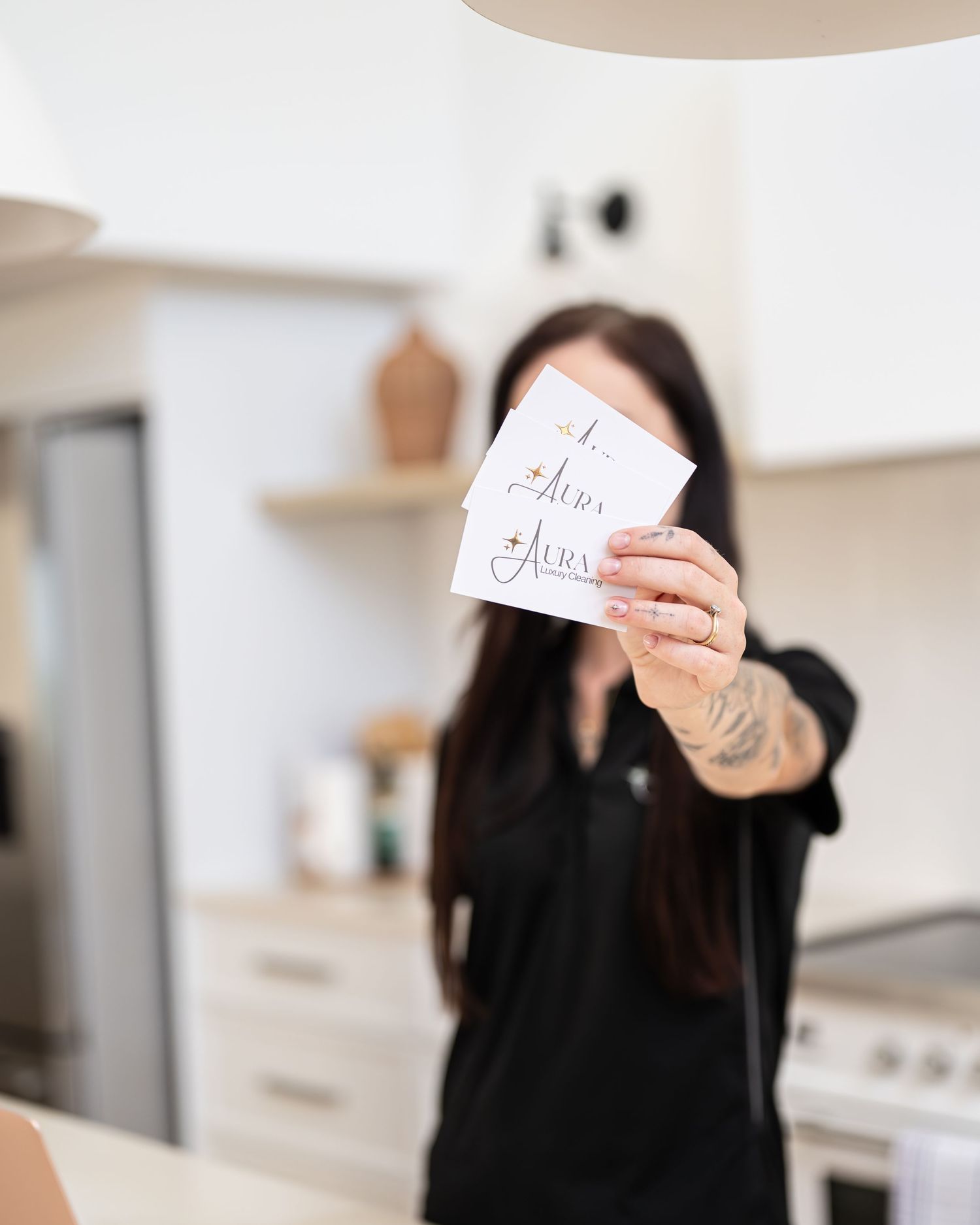 Woman in a black shirt holding up Aura branded cards in a bright, modern kitchen with soft focus background.