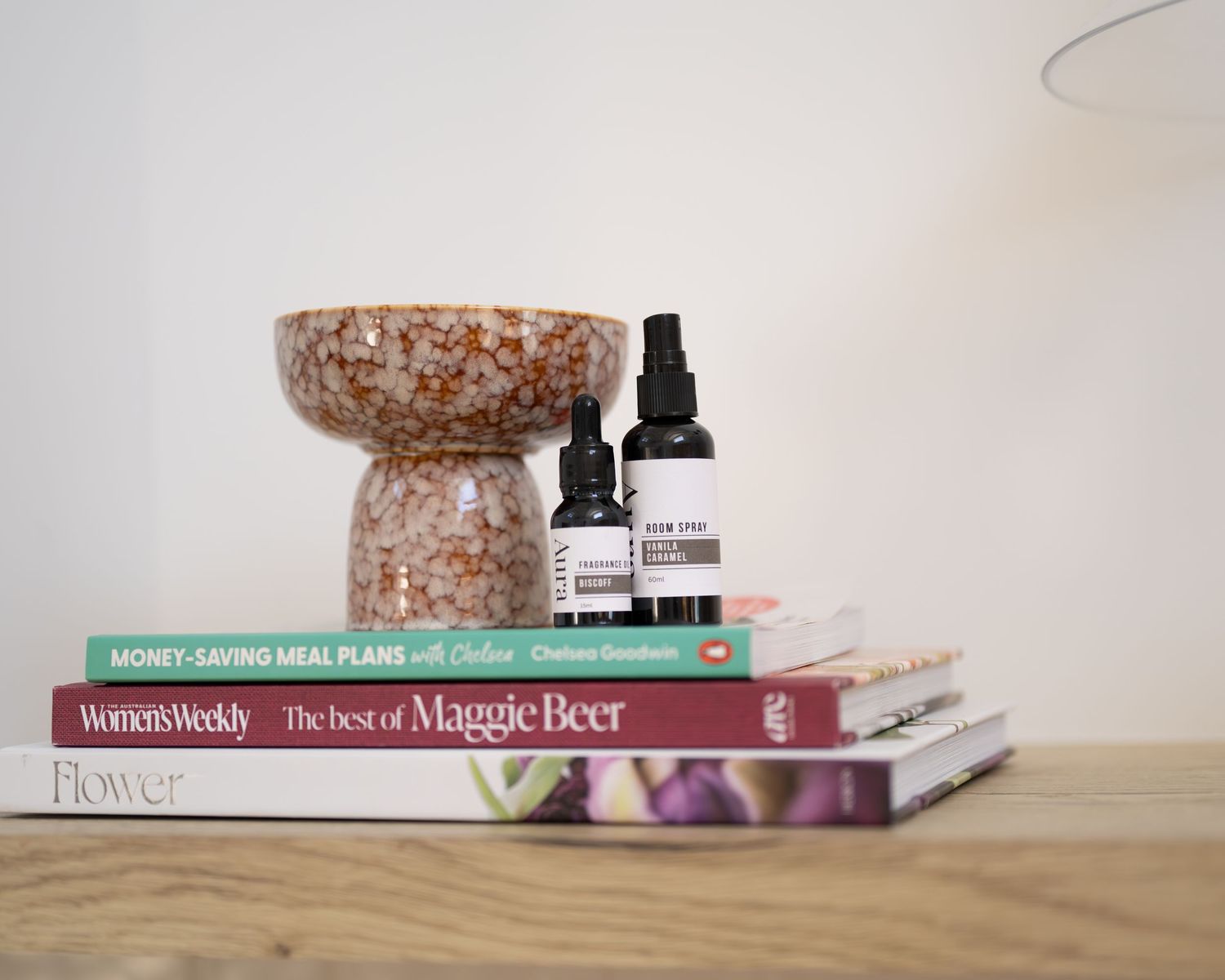 Two Aura room spray and fragrance oil bottles styled on a stack of books beside a speckled decorative bowl.