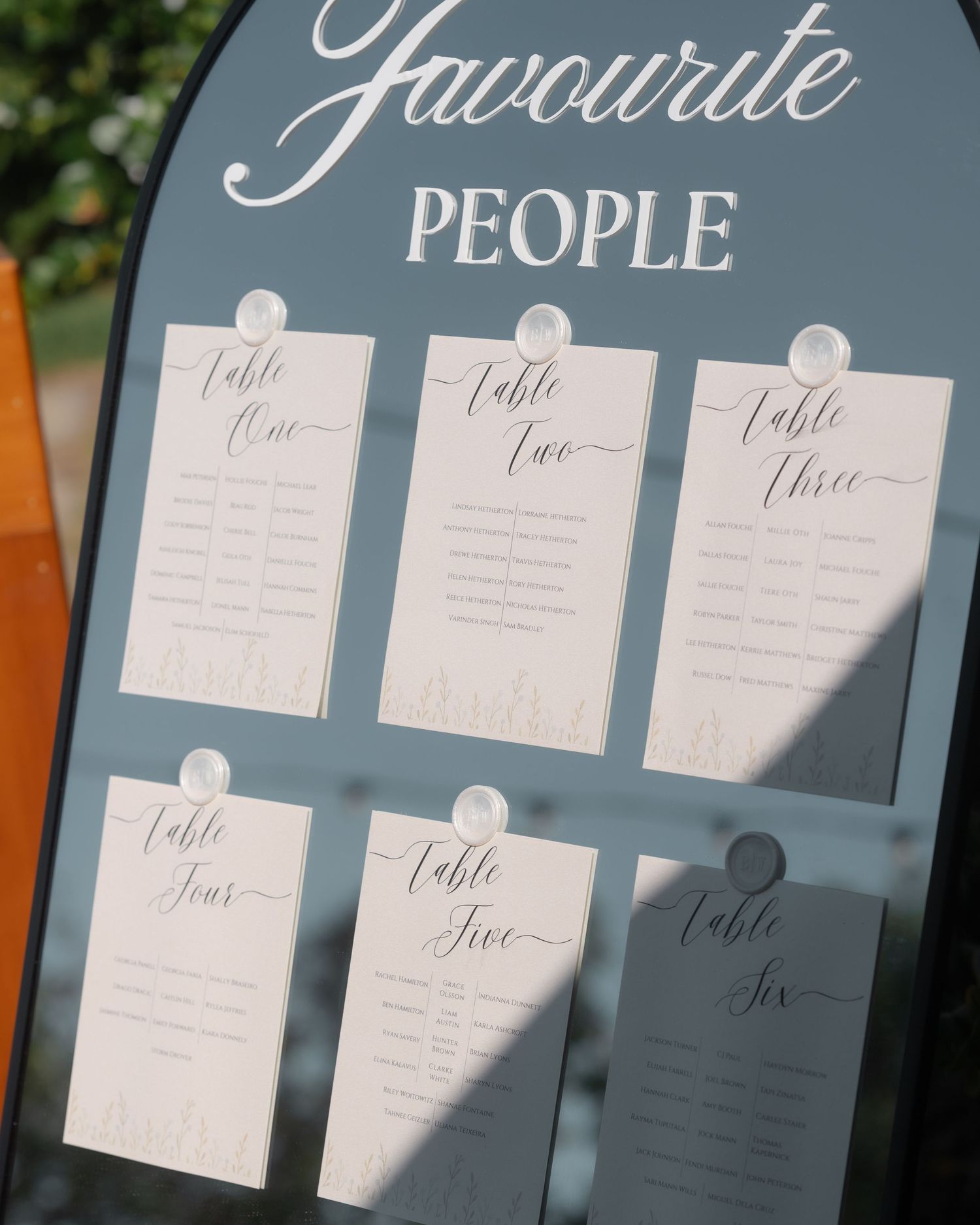 Mirrored wedding seating chart reading Favourite People with elegant script table cards for tables one through six.