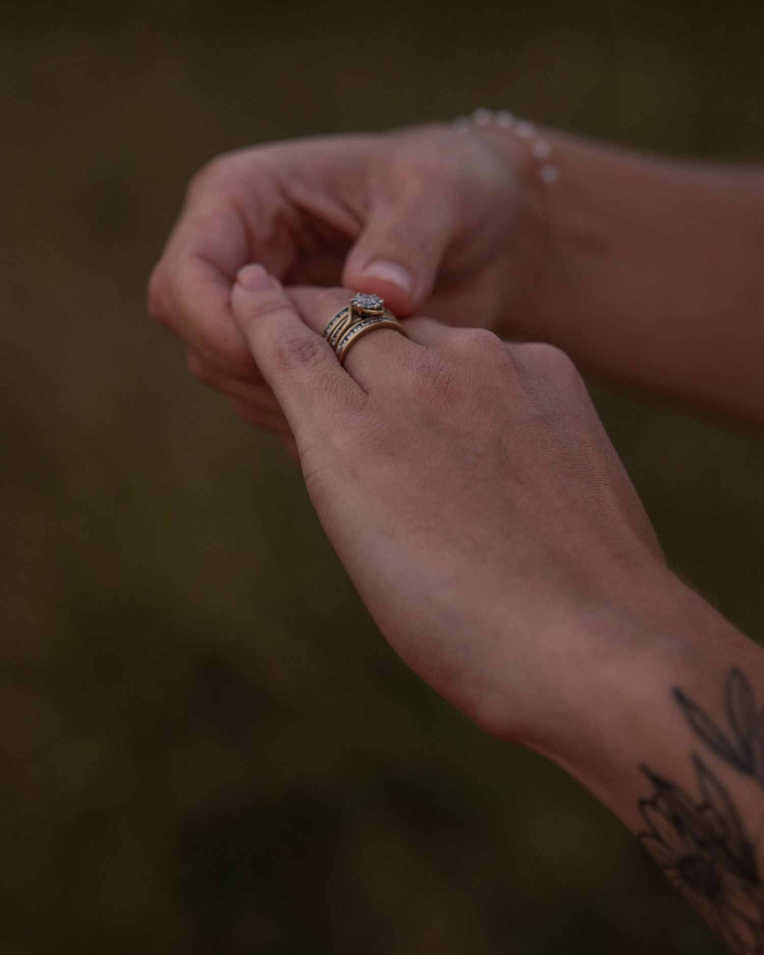 Close-up of a bride's hands adjusting a stacked gold wedding ring with a small diamond, tattoo visible on her wrist.