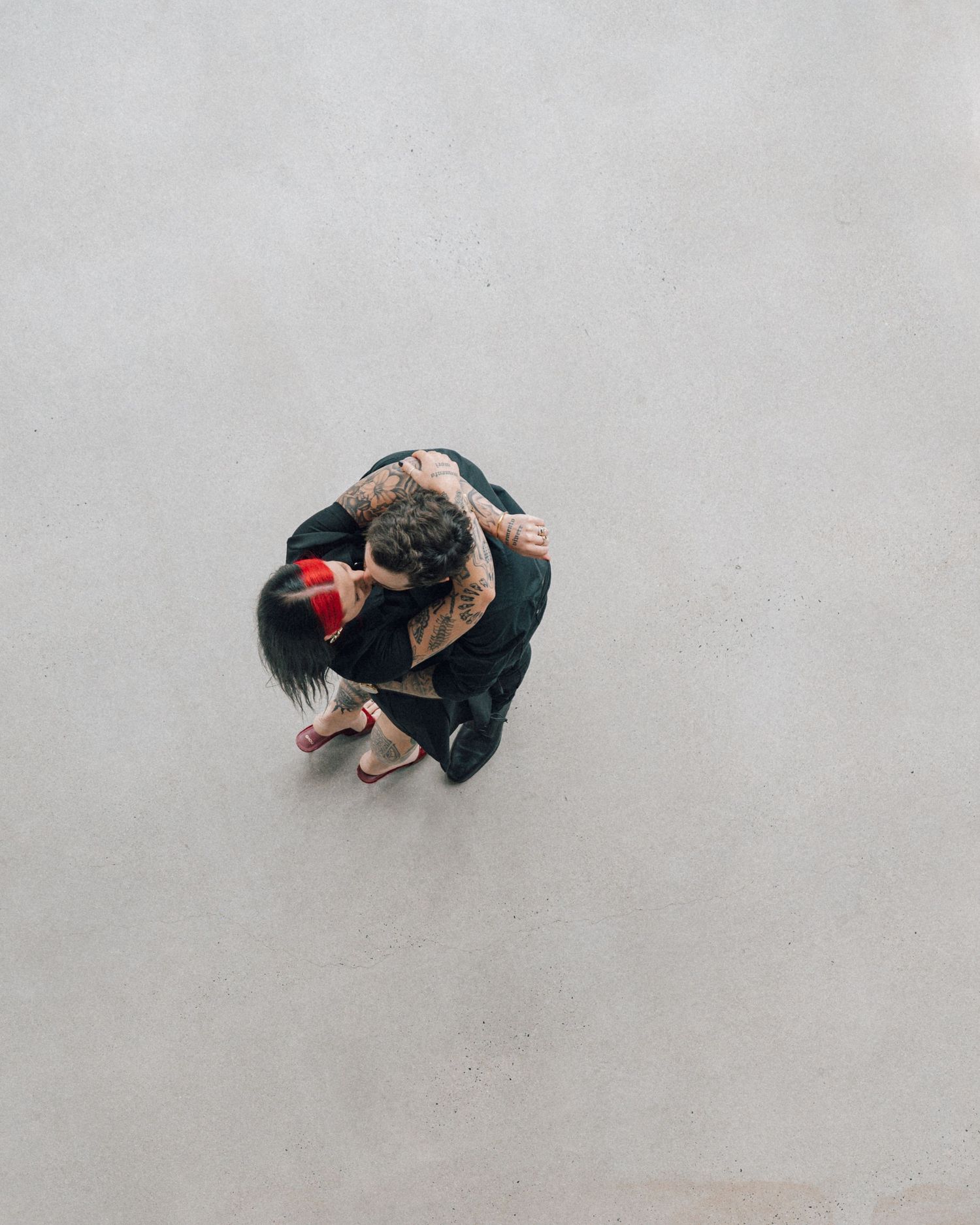 Overhead view of a couple embracing on a plain concrete floor, the woman wearing a red headband and pink sandals.