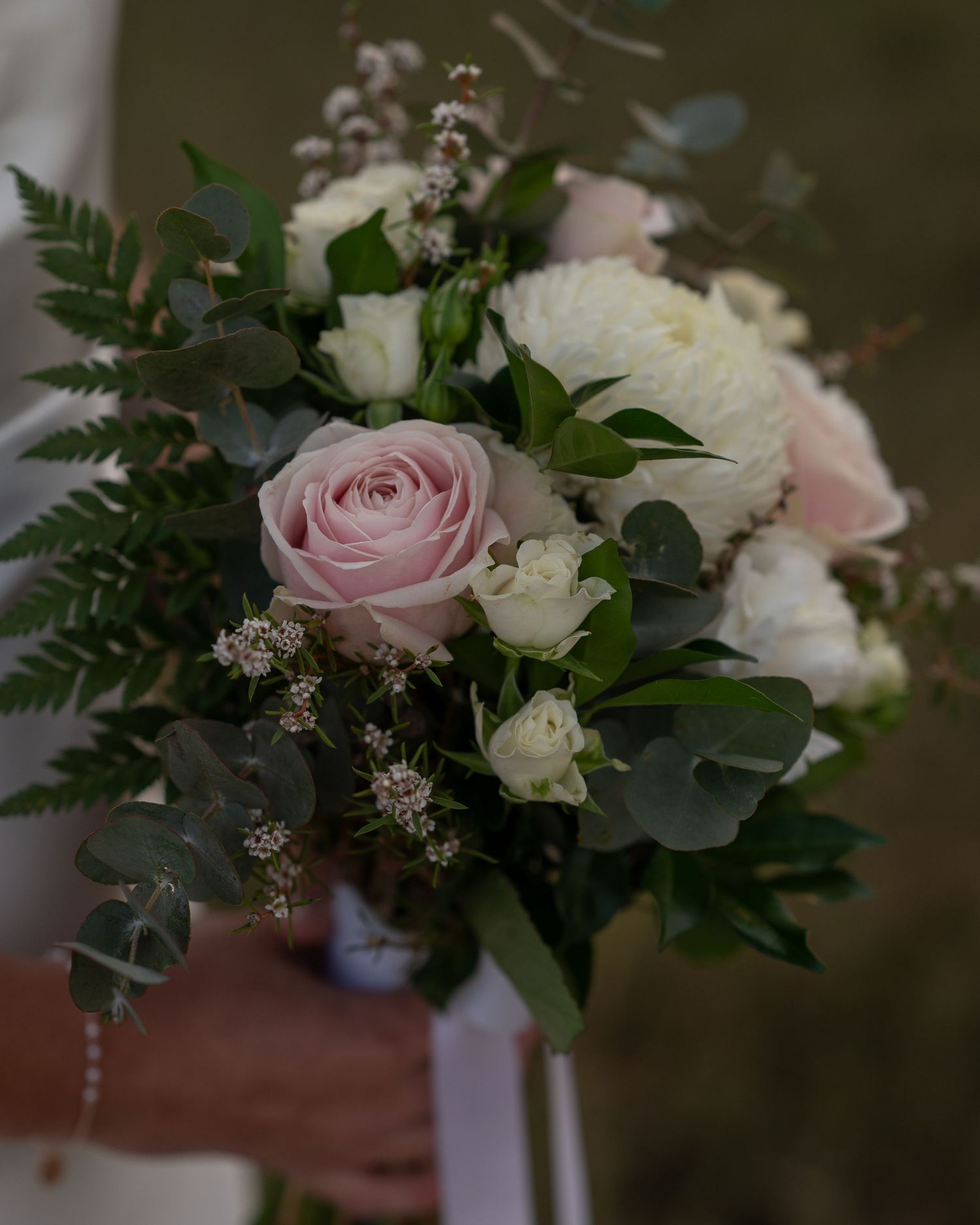 Close-up of a bridal bouquet with blush pink roses, white blooms, ferns and eucalyptus leaves.