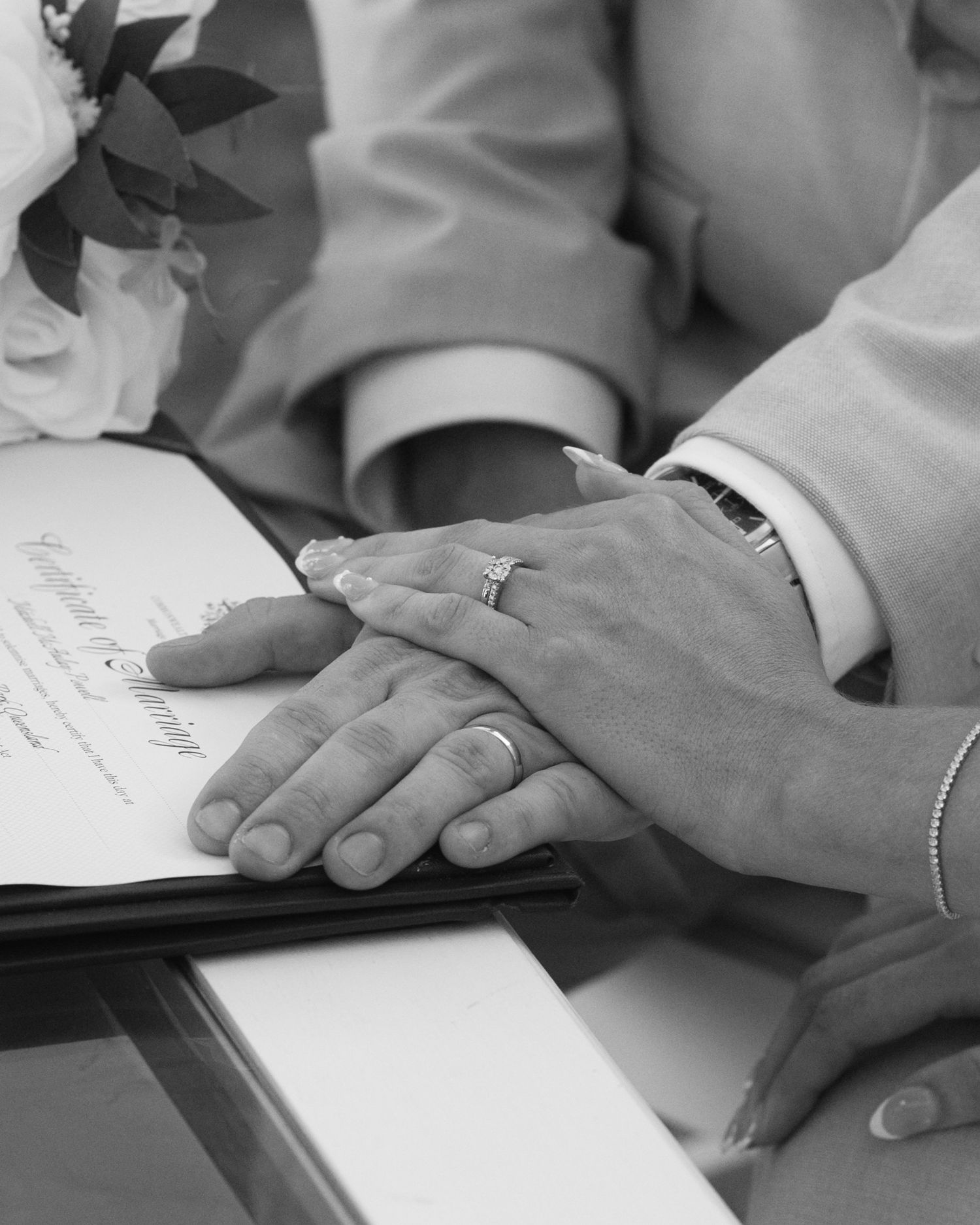 Black and white close-up of a couple's hands with wedding rings resting on the marriage certificate.