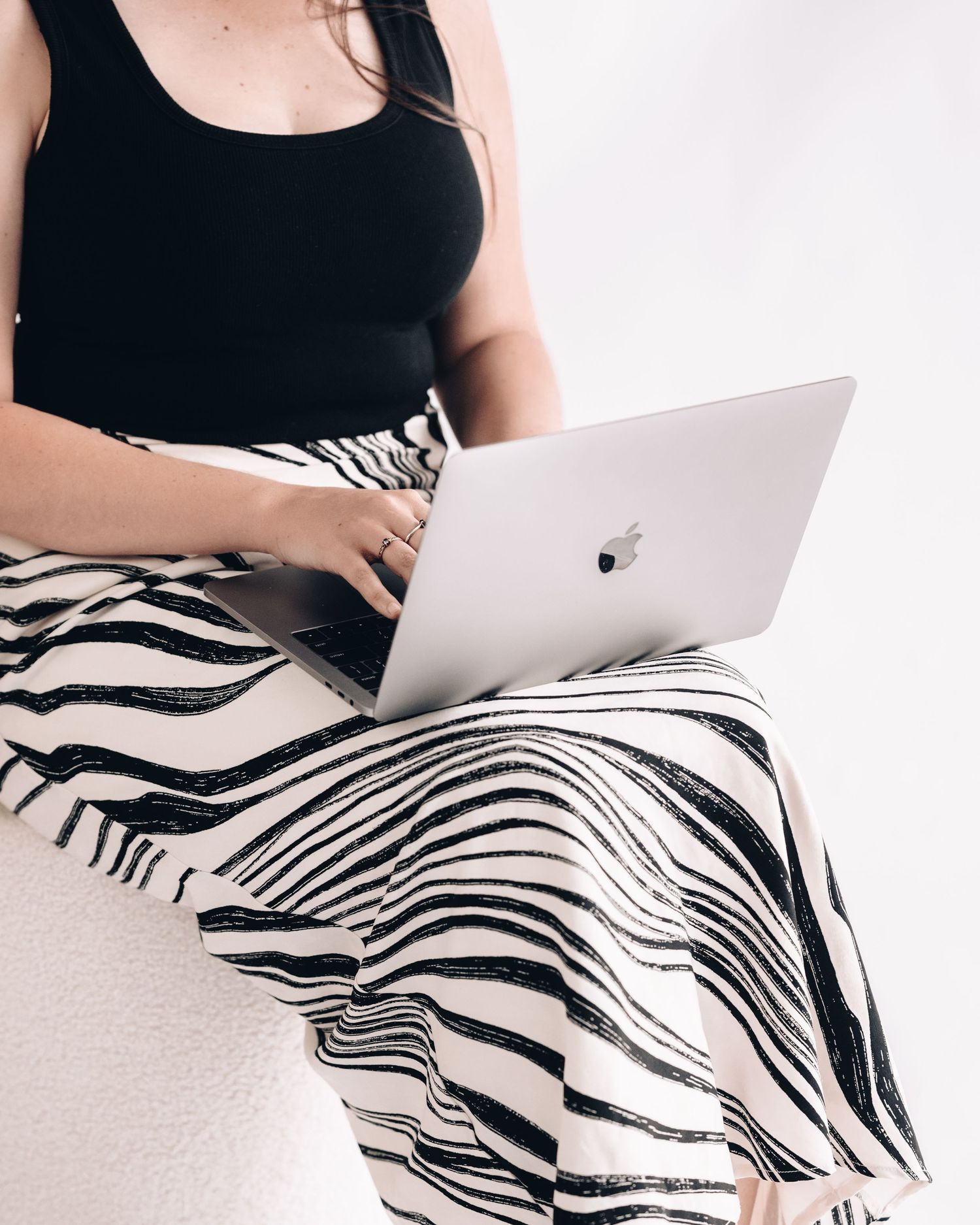Close-up of a woman in a black tank top and zebra-print skirt typing on a silver laptop resting on her lap.