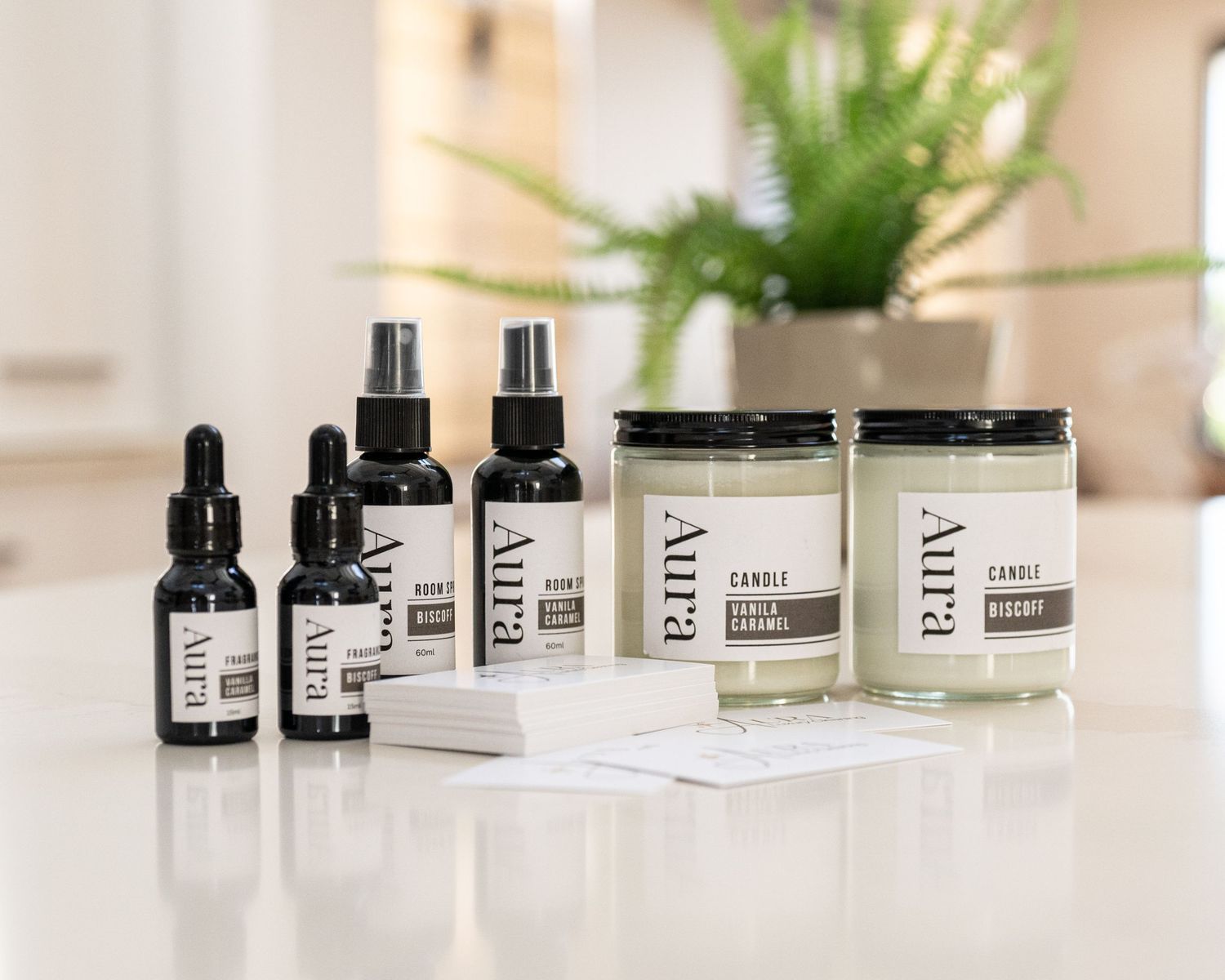Aura aromatherapy set featuring two dropper oil bottles, two spray mists, and two scented candle jars on a white table near a green plant.