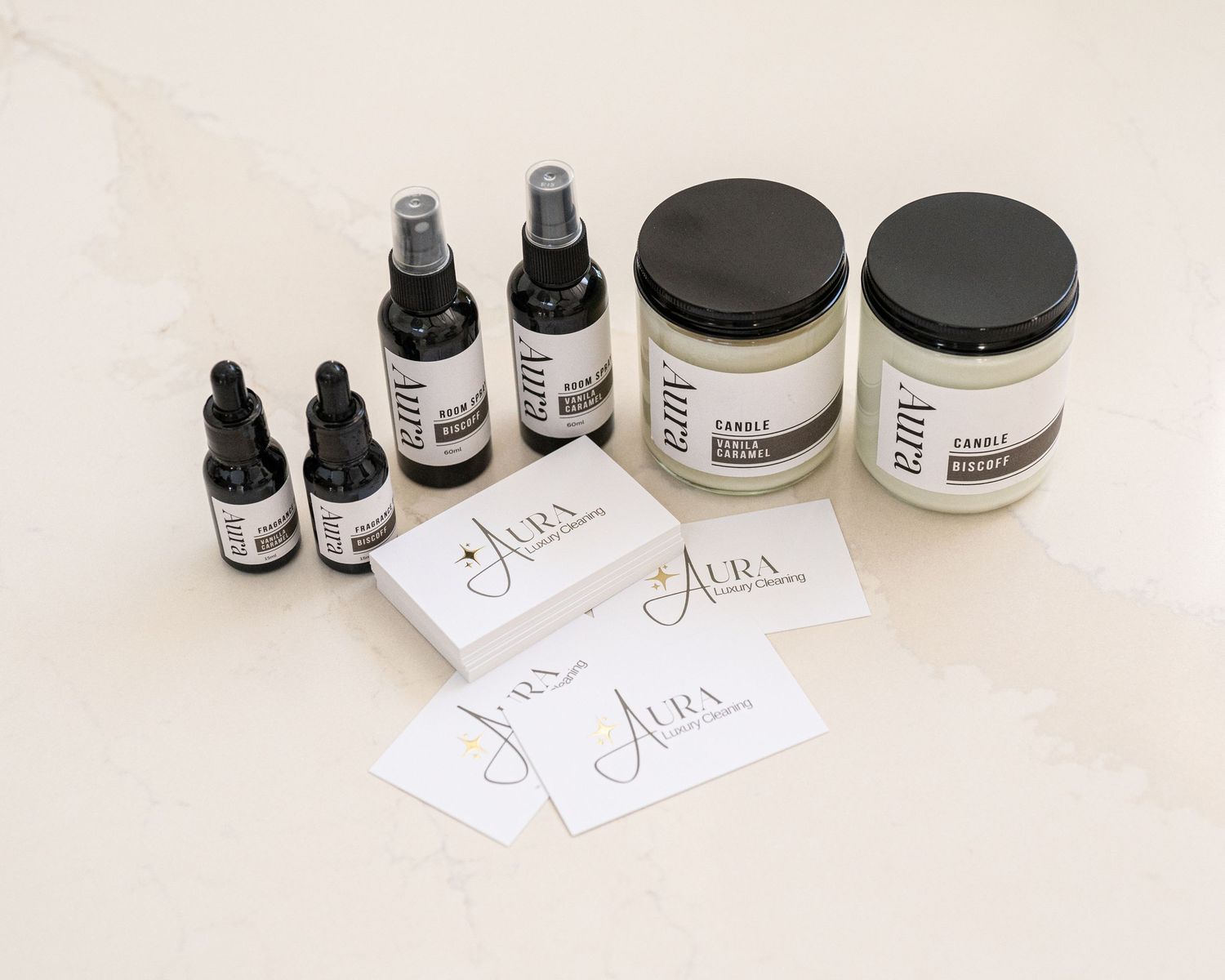 Aura candles, fragrance oils, room sprays and branded business cards arranged on a white marble surface.