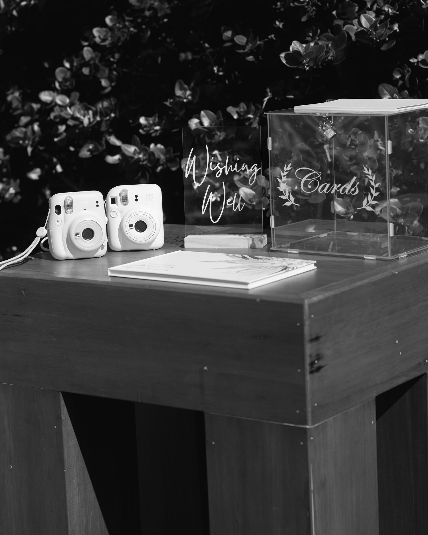 Black and white wedding gift table with two instant cameras, a wishing well sign, a guest book and a clear cards box.