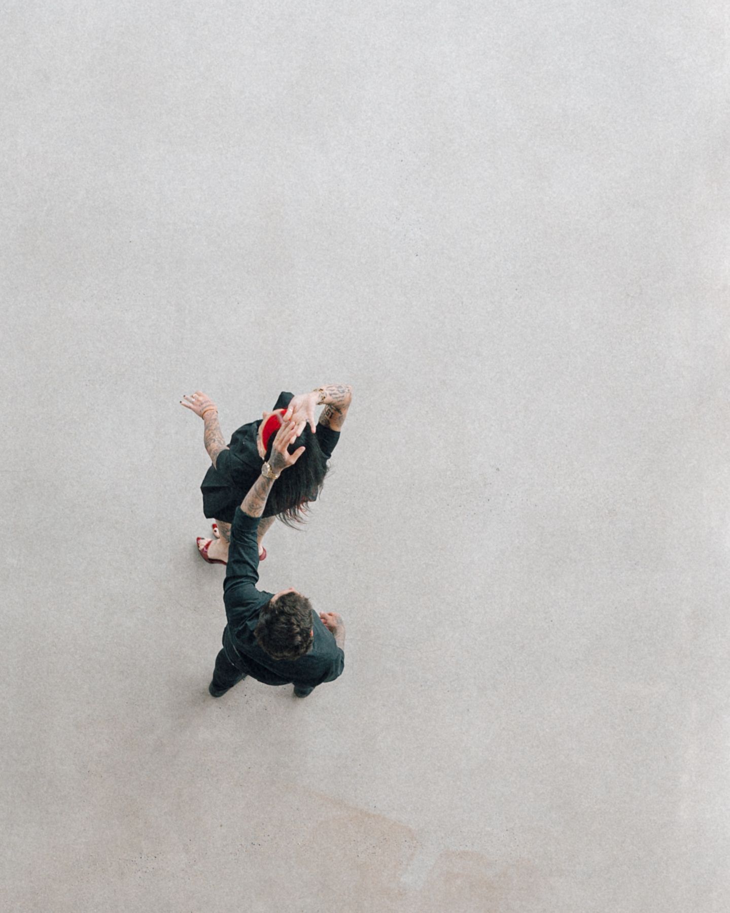 Overhead view of a couple in dark clothing dancing together on a plain concrete floor.