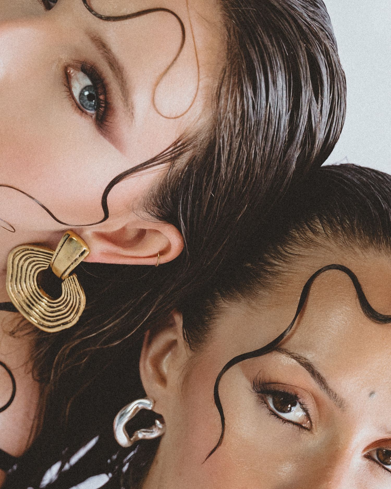 Close-up of two women's eyes and faces with wet-look hair, bold gold earrings and curving black line makeup designs.