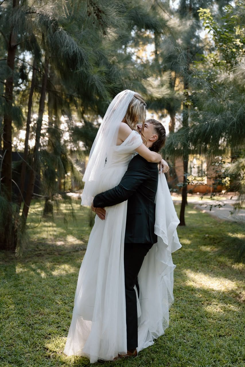 Groom lifts his veiled bride in a romantic embrace surrounded by tall pine trees on their wedding day.