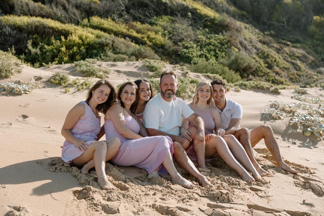 Happy family of six sitting together on sandy beach dunes in warm golden sunlight.