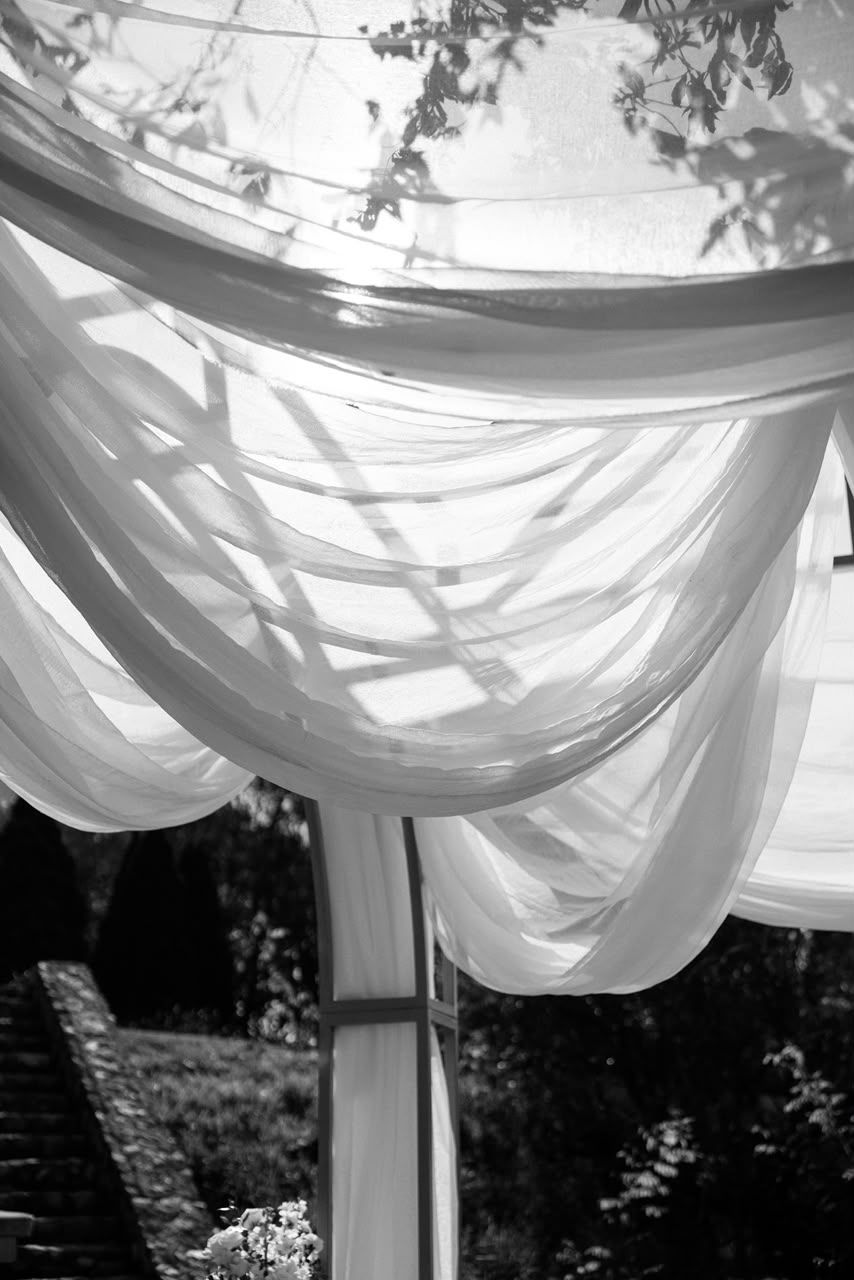 Black and white artistic shot of flowing white fabric wedding arch canopy billowing in the breeze outdoors.