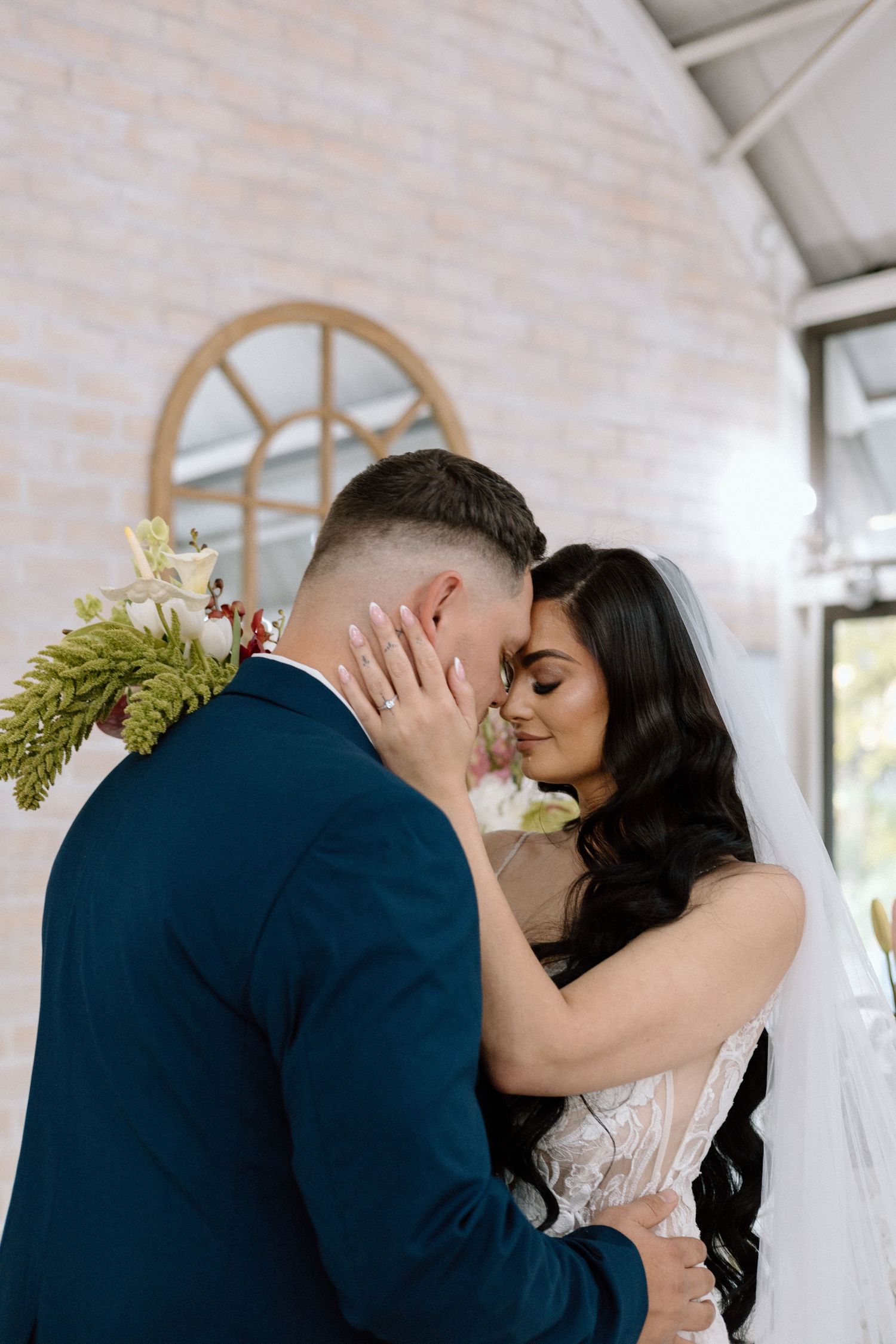 Bride and groom share an intimate forehead touch moment during their wedding ceremony in an elegant white venue.
