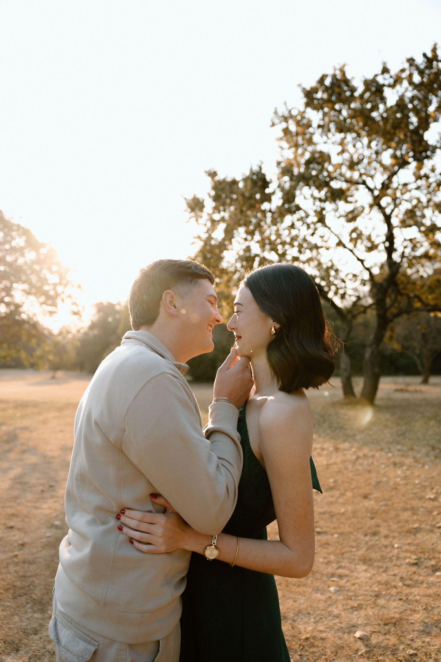 Couple sharing a romantic moment at golden hour in a sunlit field with trees in the background.