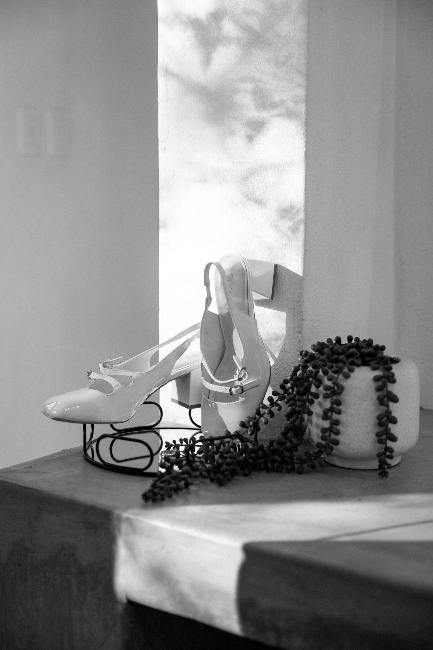 Black and white photo of elegant bridal heels and floral accessories arranged on a wooden surface.