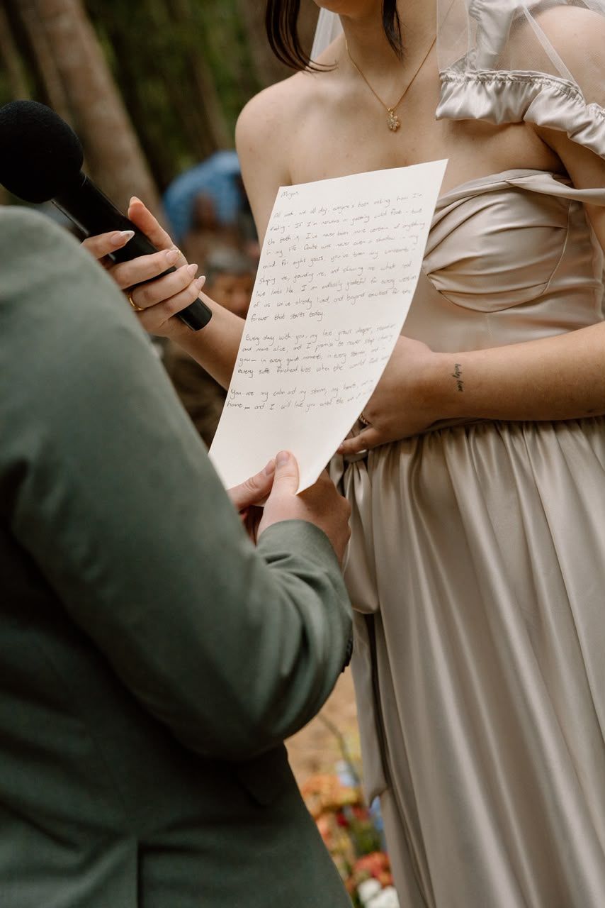 Bridesmaid in a champagne off-shoulder gown reads handwritten vows during an outdoor woodland ceremony.