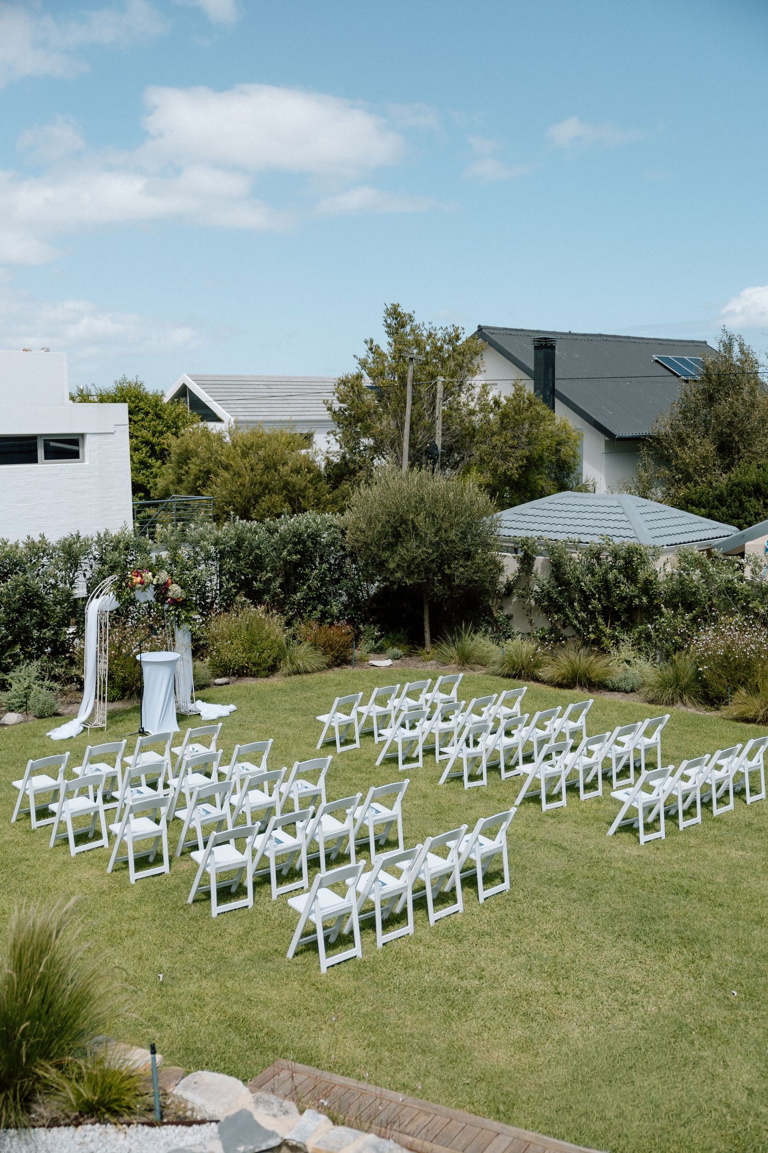White chairs arranged in rows on a green lawn for an outdoor wedding ceremony setup on a sunny day.