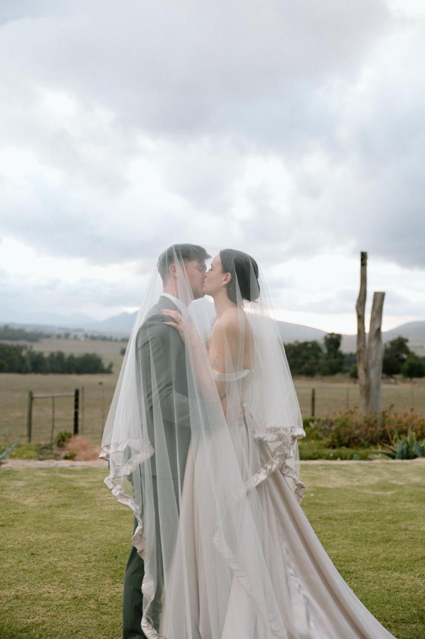 Bride and groom sharing a kiss under a flowing white veil with scenic mountain backdrop on their wedding day.