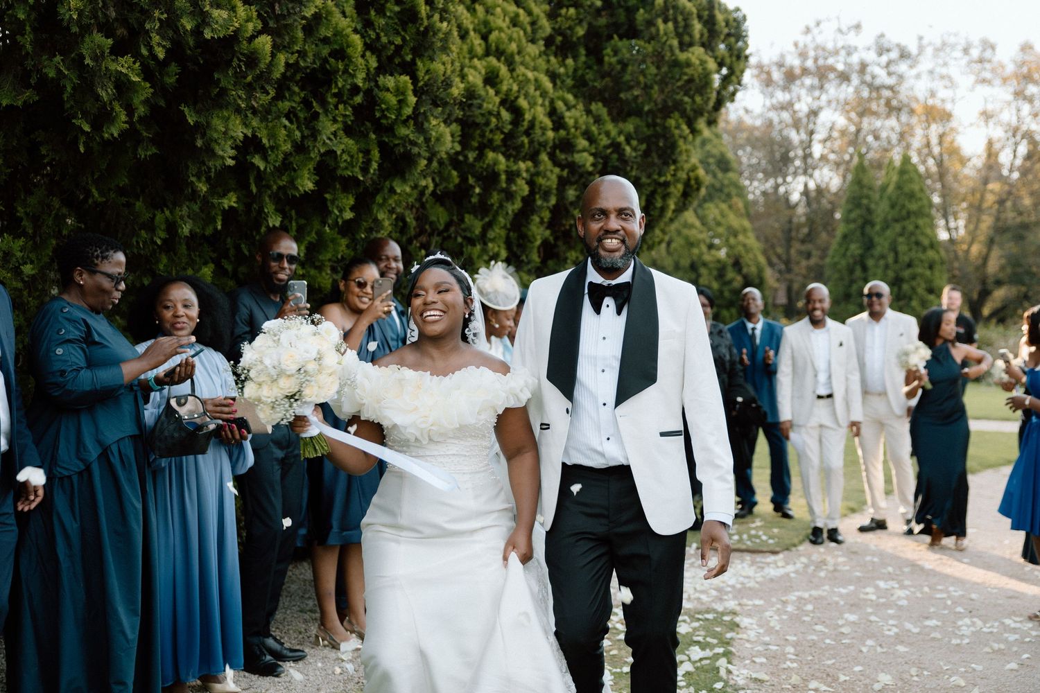 Bride and groom walk joyfully down the aisle at outdoor wedding ceremony with bridal party in teal dresses.