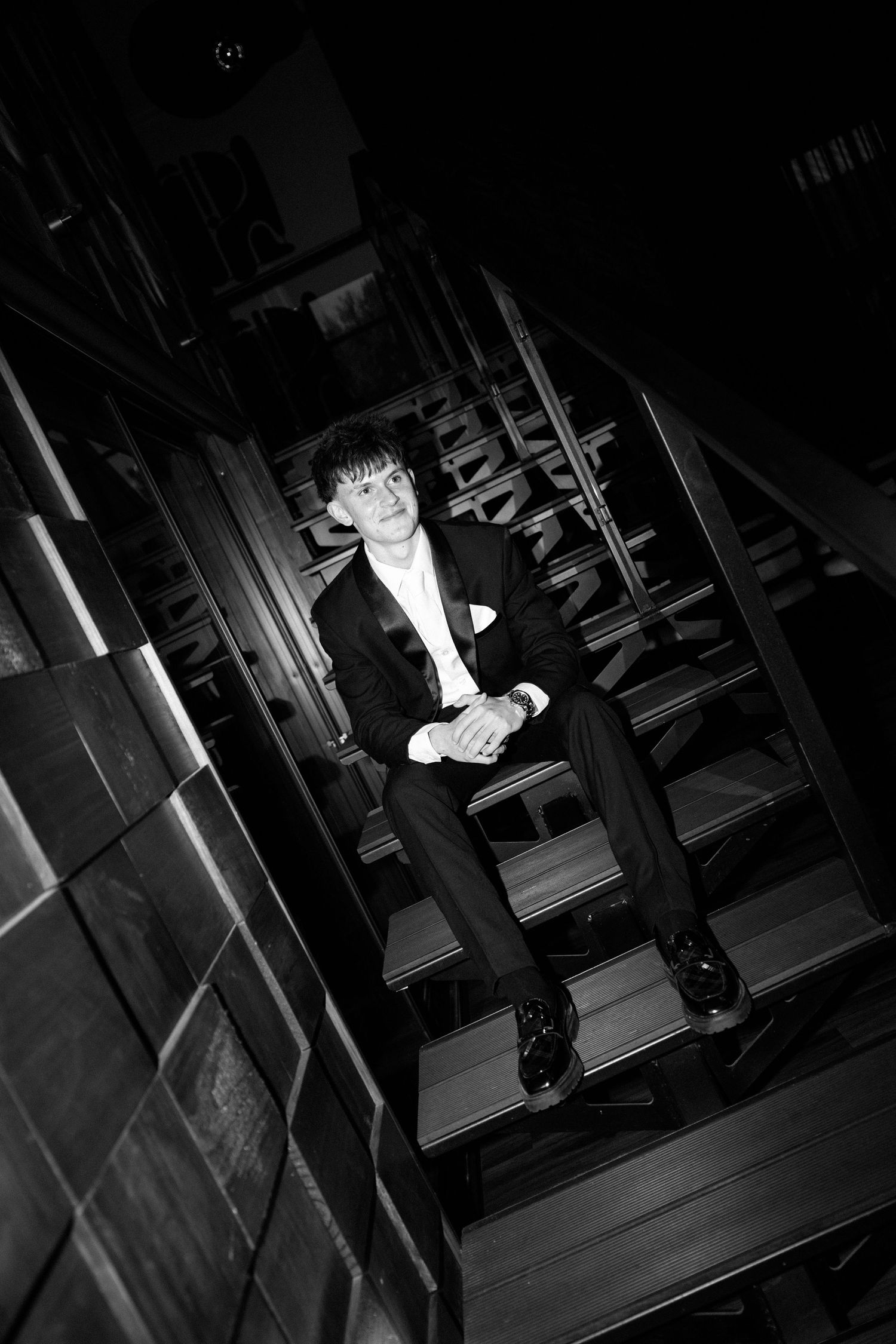 Young man in black suit sitting on wooden stairs, black and white portrait photography.