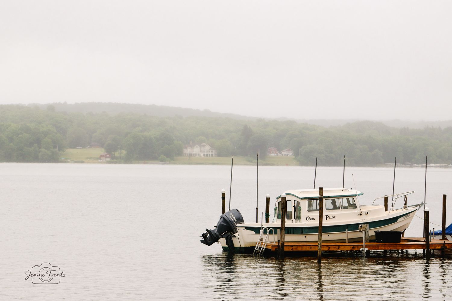 Misty foggy morning with a white fishing boat docked at a pier on a calm lake.