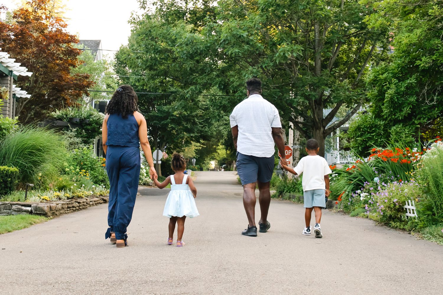 Family of four walking hand in hand down a garden path surrounded by colorful flowers.