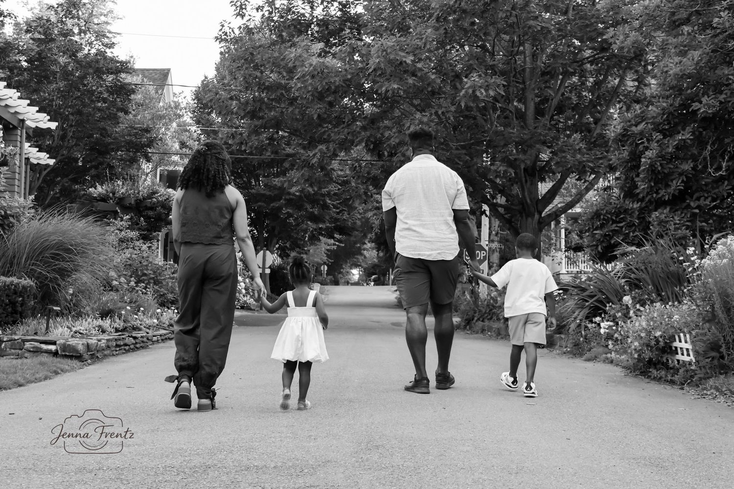 Black and white photo of a family walking together down a tree-lined path in a park.