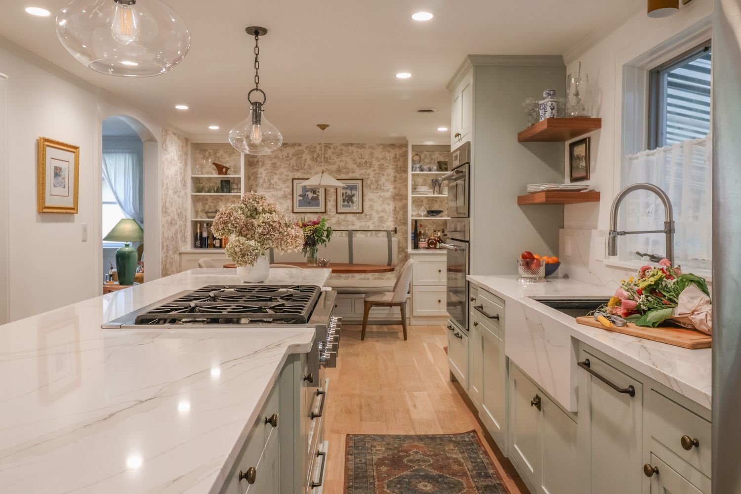Bright farmhouse kitchen with sage green cabinets, white quartz countertops, open shelving, and pendant lights.