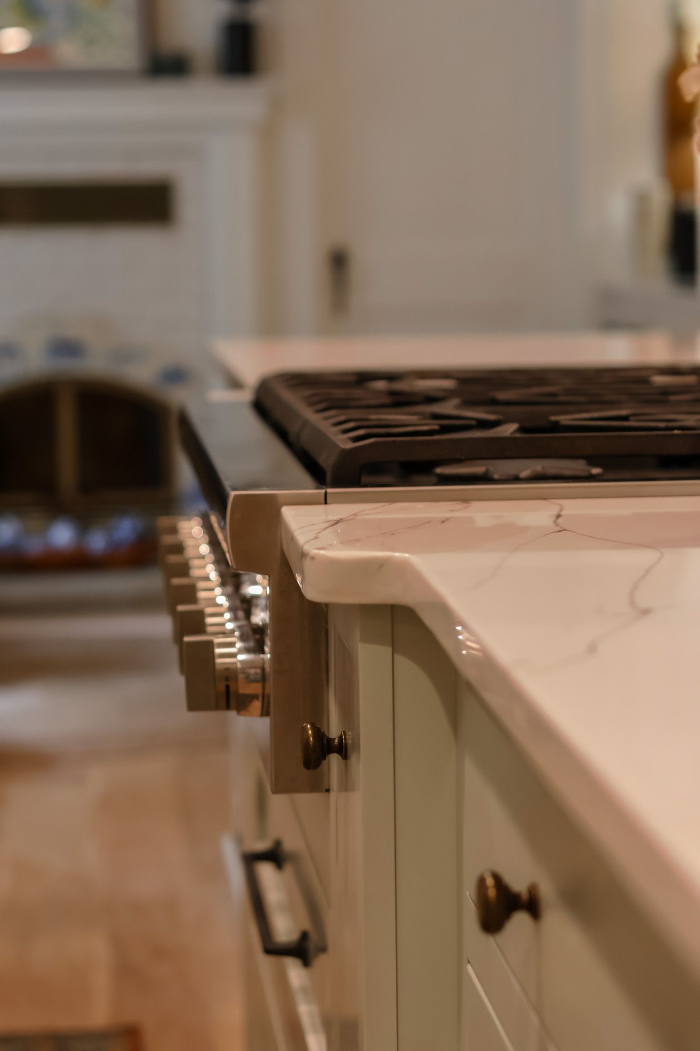 Close-up of white marble kitchen island countertop with built-in gas cooktop and sage green cabinetry.