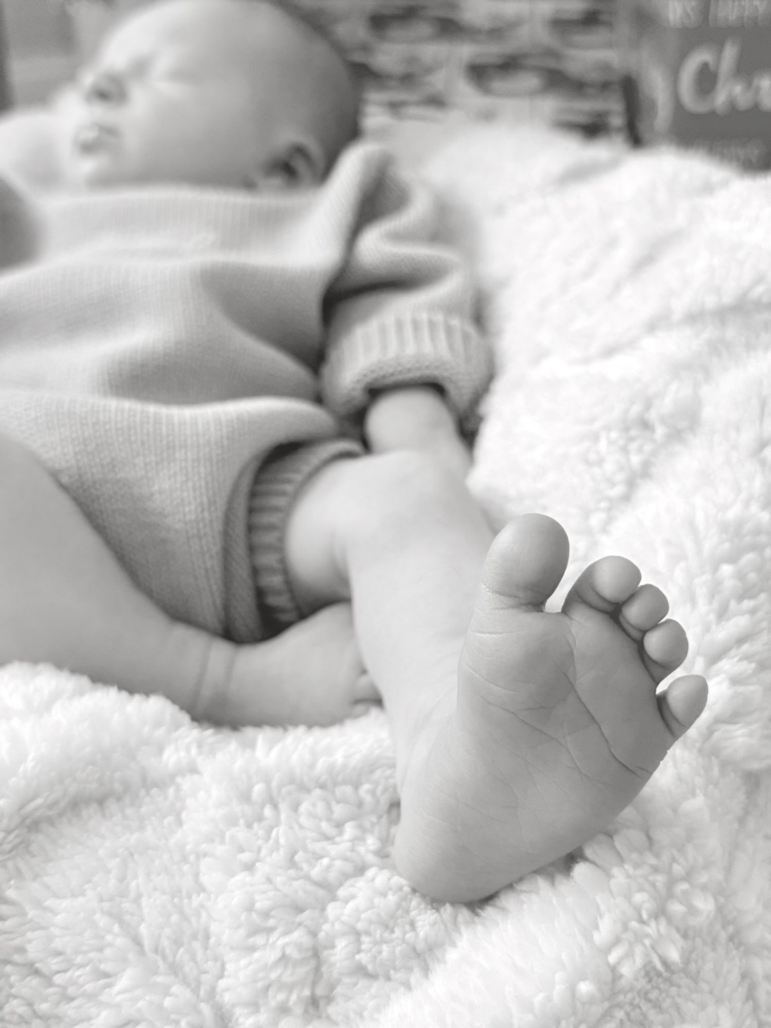 Black and white close-up of a newborn baby's tiny foot resting on a soft white blanket.