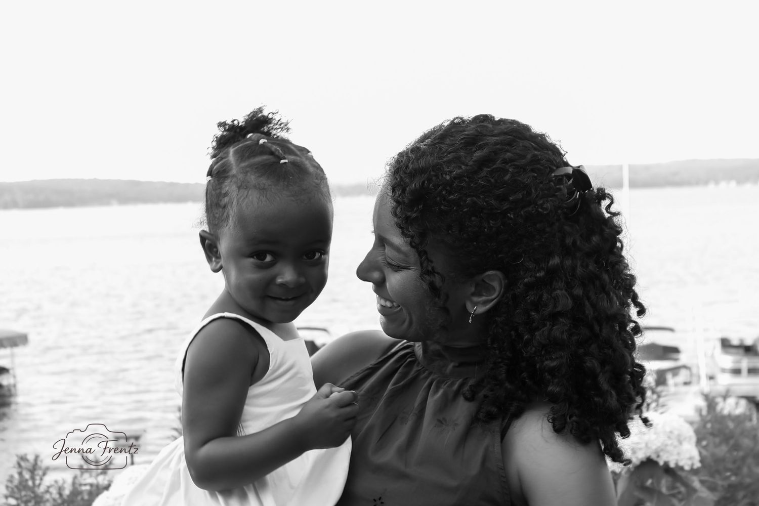 Black and white photo of a mother and young daughter sharing a tender moment by a lake.