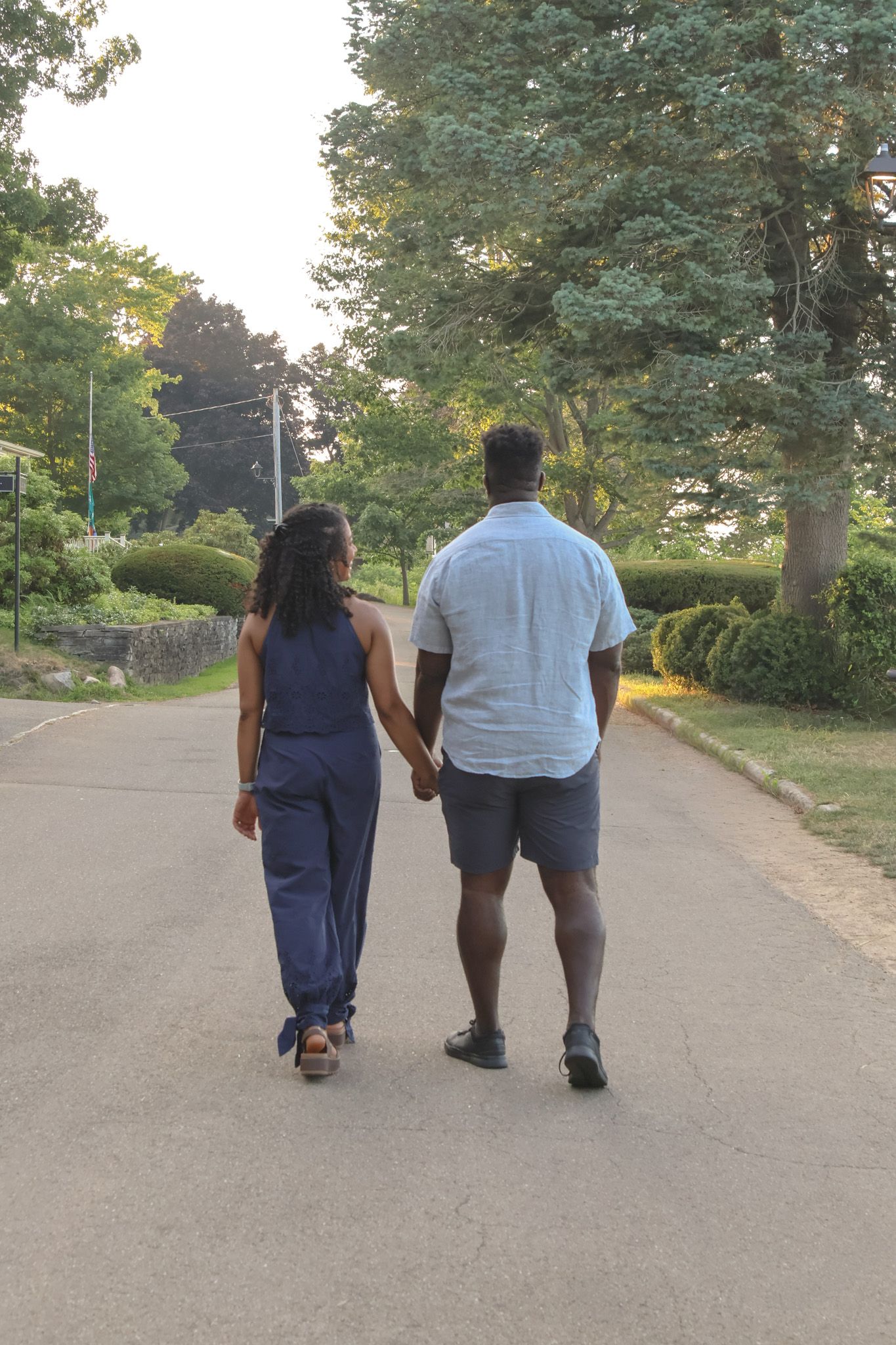 Couple holding hands walking down a peaceful tree-lined road at golden hour sunset.