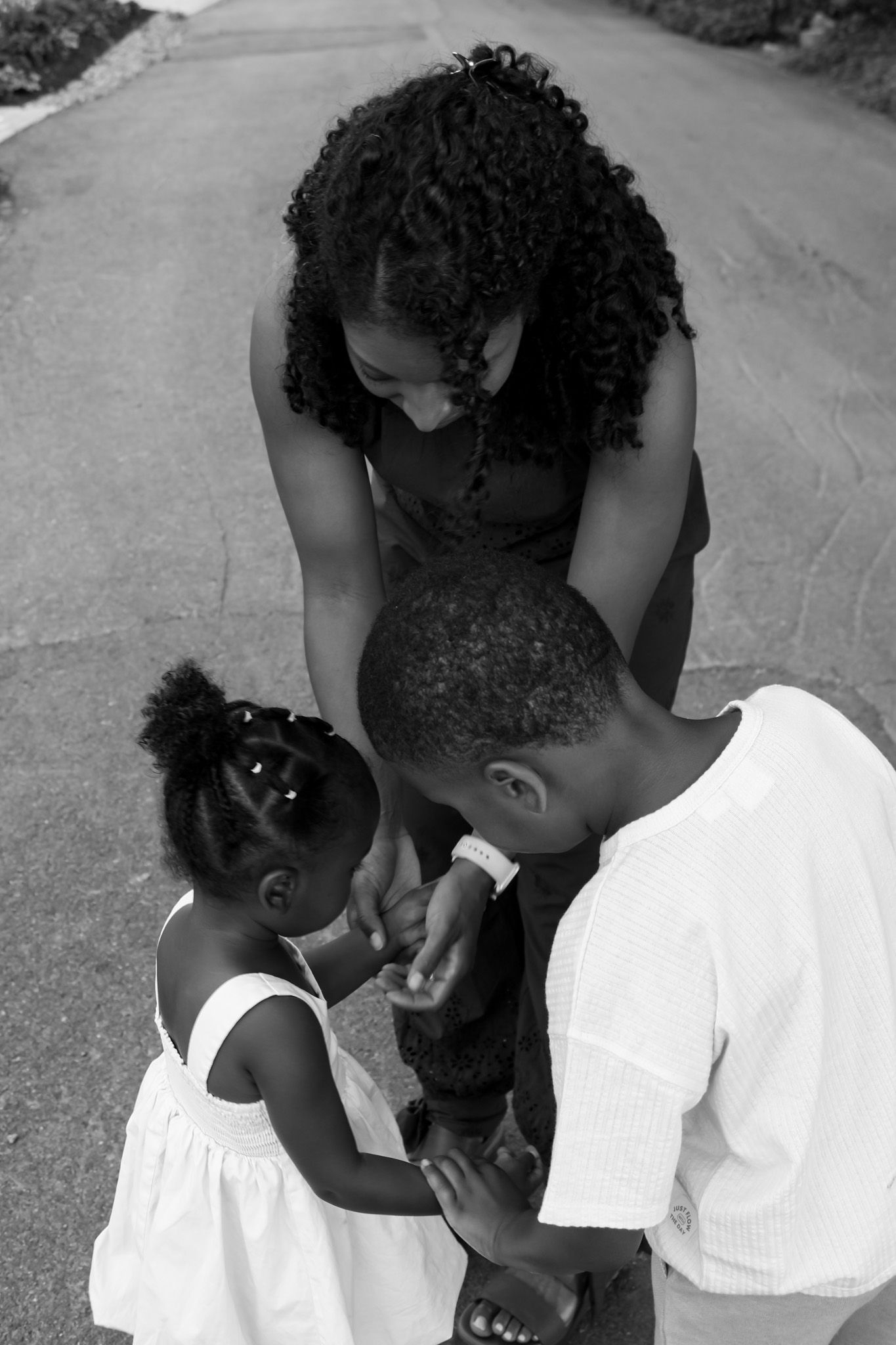 Black and white overhead photo of a mother bending down to her two young children on a pathway.