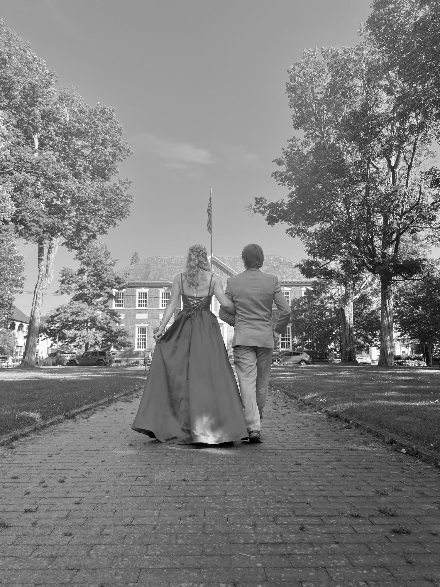Black and white photo of a couple walking hand-in-hand down a brick path toward a historic building.