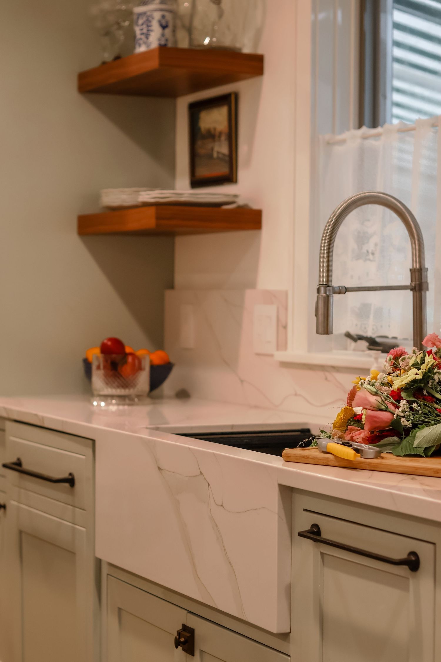 Elegant white kitchen with marble farmhouse sink, wood shelves, and fresh vegetables.