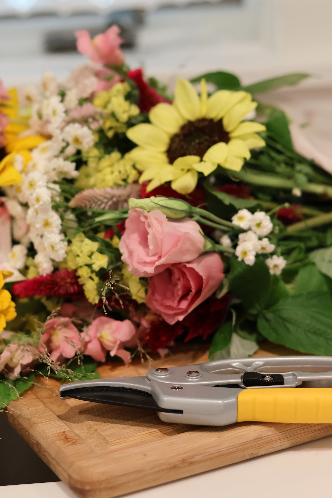 Fresh colorful flower bouquet with sunflowers and roses on cutting board with yellow-handled garden shears.
