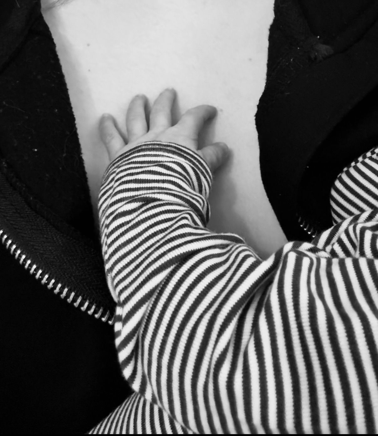 Black and white close-up of a baby hand in striped onesie resting on an adult chest.