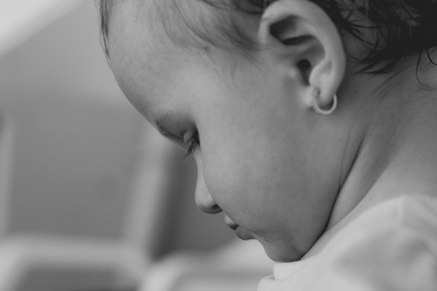 Black and white close-up profile of a baby girl with a small gold hoop earring looking down.