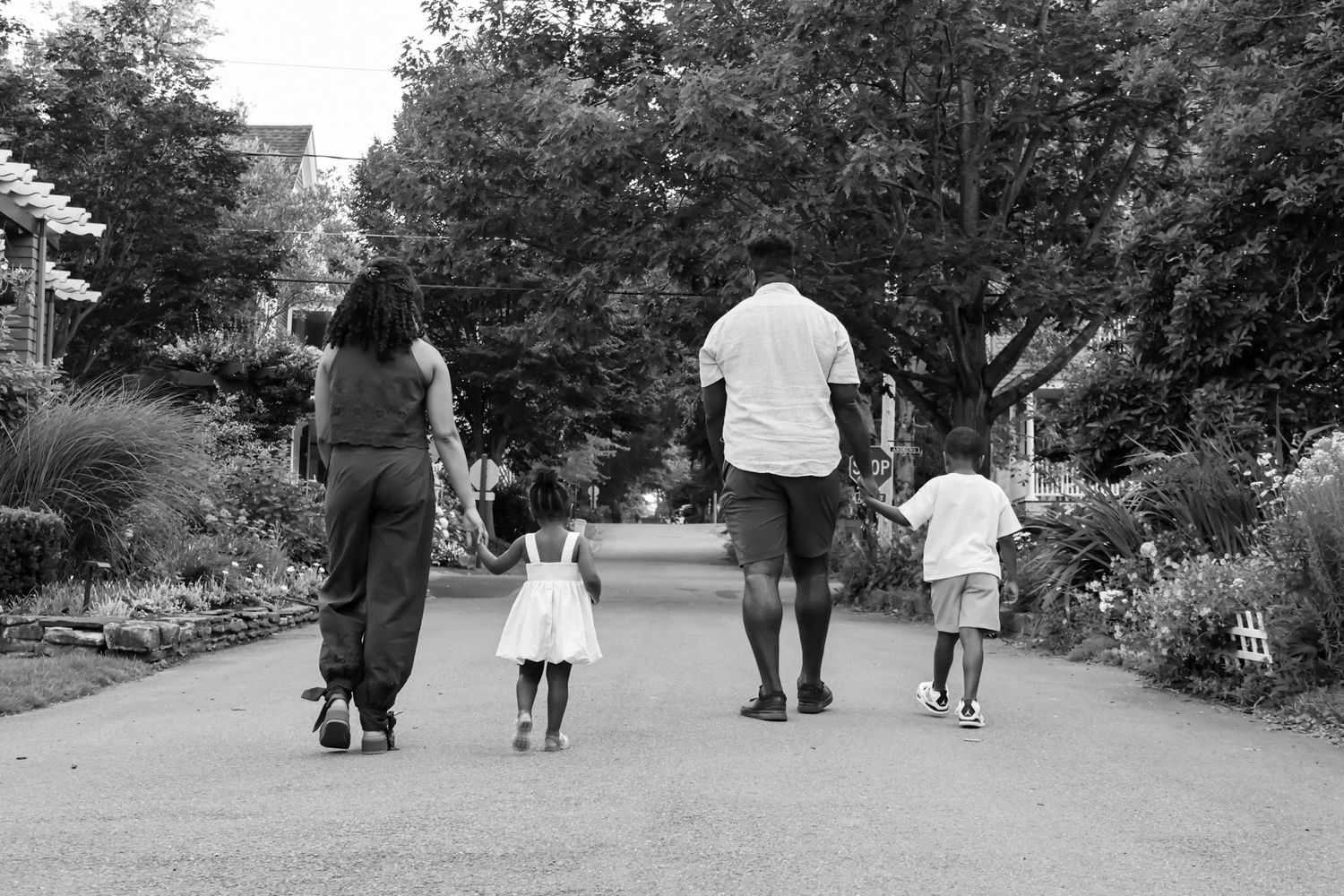 Black and white photo of a family of four walking together down a tree-lined park pathway.