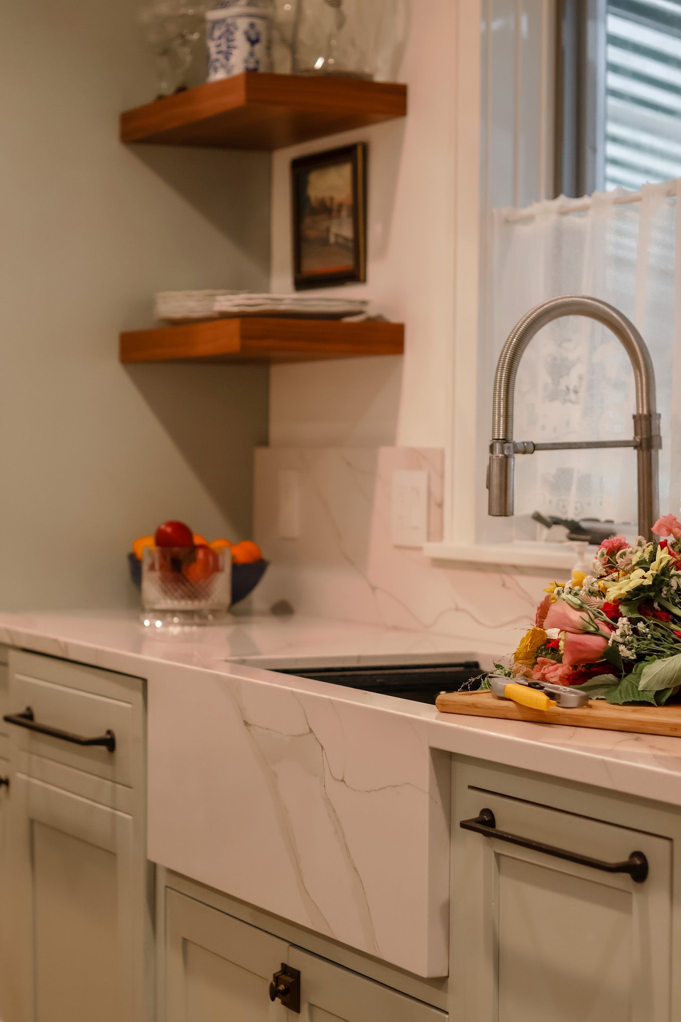 Farmhouse apron sink with marble countertop, wood floating shelves, and fresh produce on cutting board.
