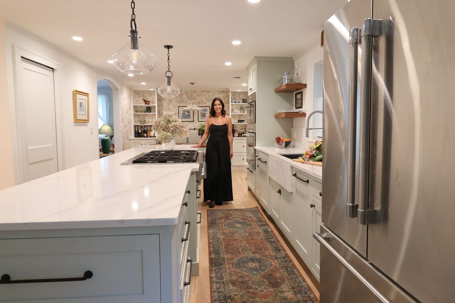Woman in black dress standing in a modern renovated kitchen with white countertops.