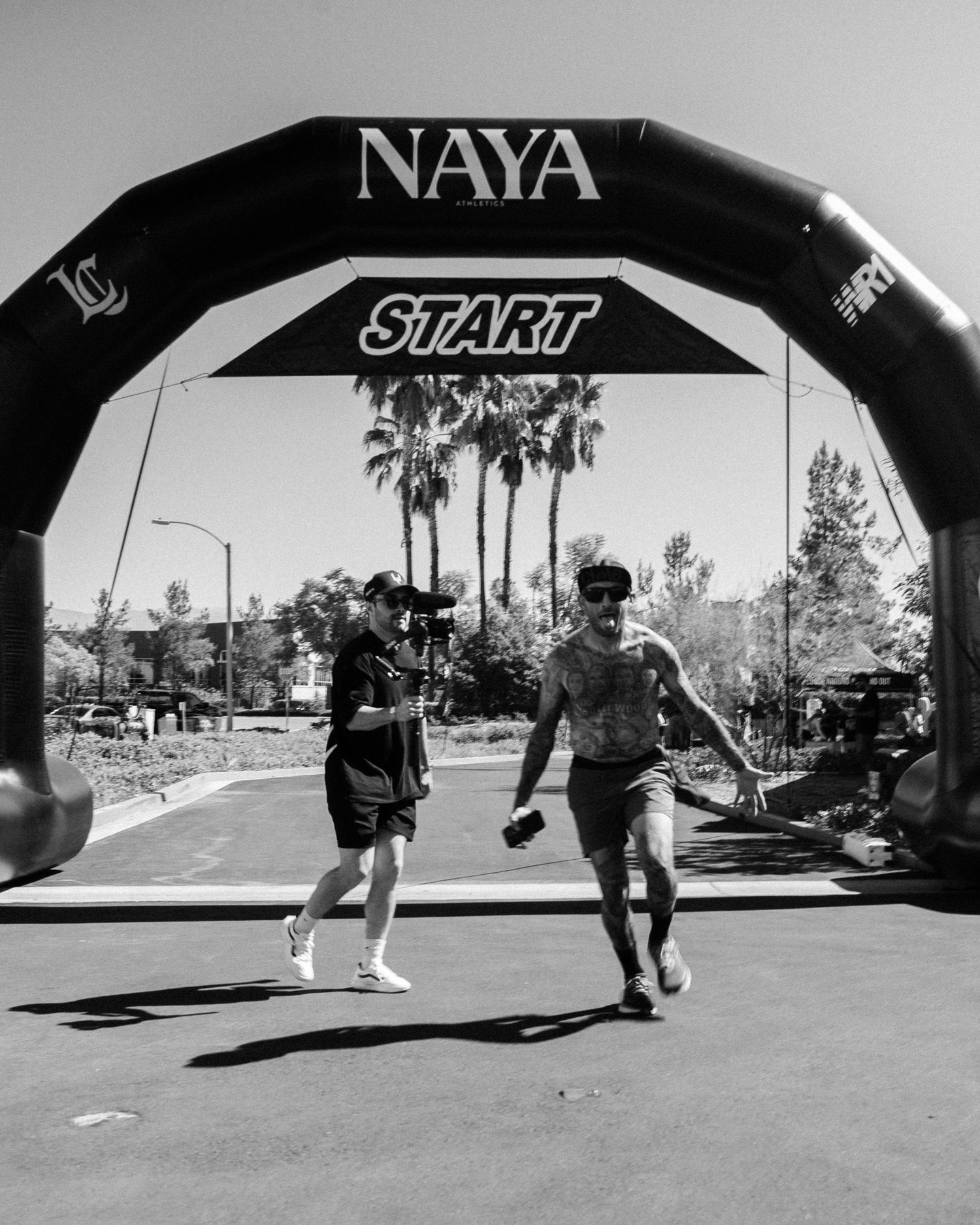 Two runners cross the start line under a NAYA branded inflatable arch at an outdoor race event.