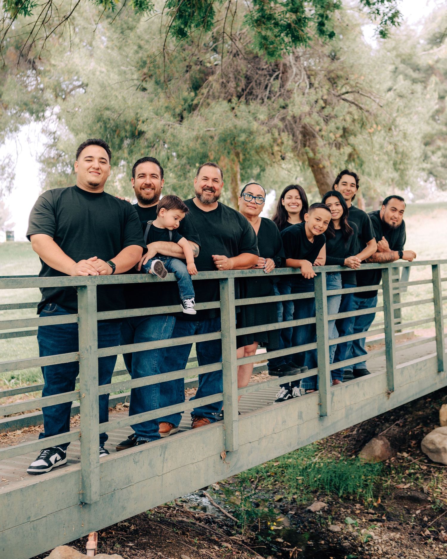 Large family group posing on bridge wearing matching black shirts and jeans.
