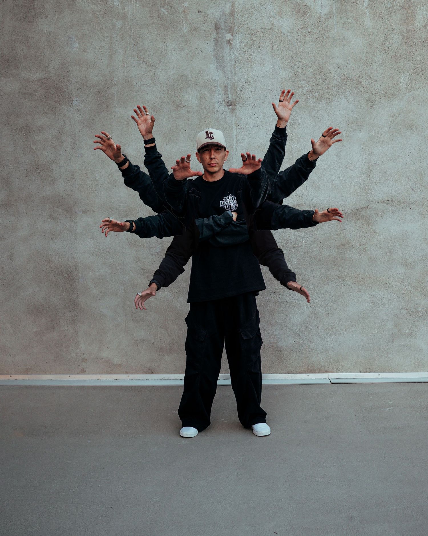 Creative photo of man in black outfit with multiple hands radiating outward against concrete wall.