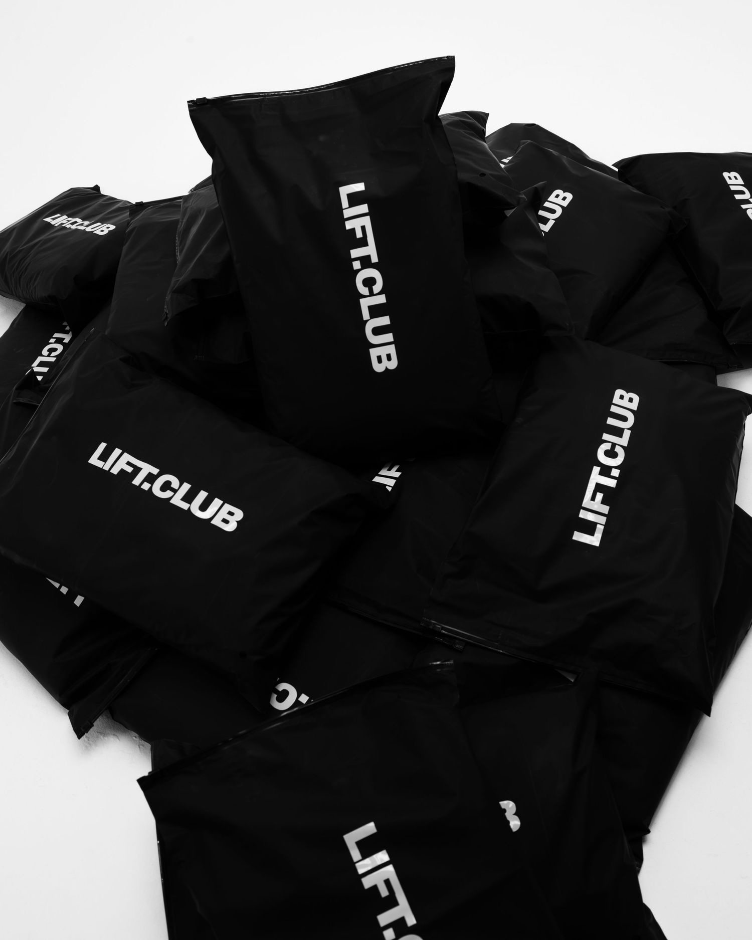 Pile of black LIFT.CLUB branded packaging bags stacked together on white background.