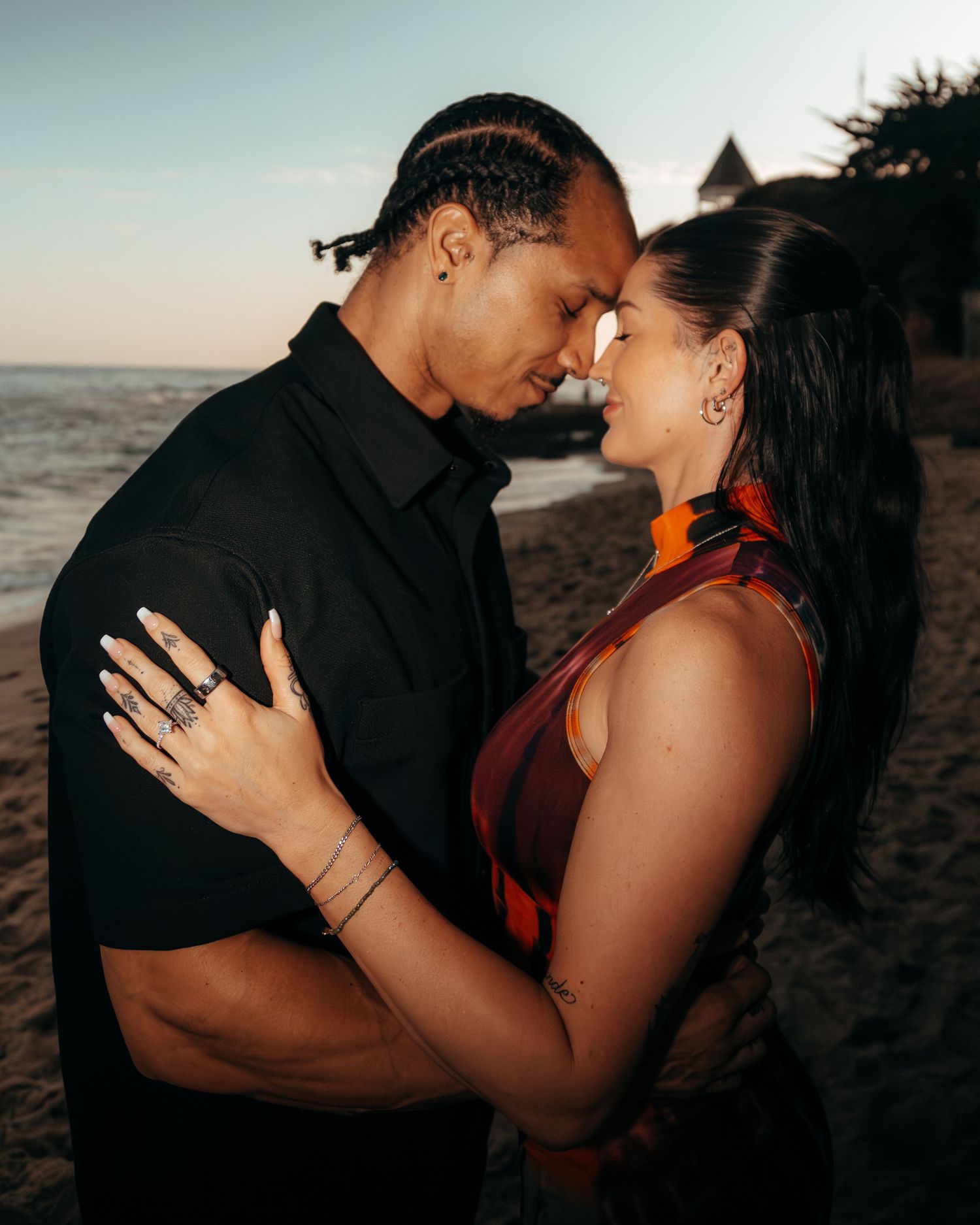 Romantic couple embracing on a beach at sunset, touching foreheads in an intimate moment.